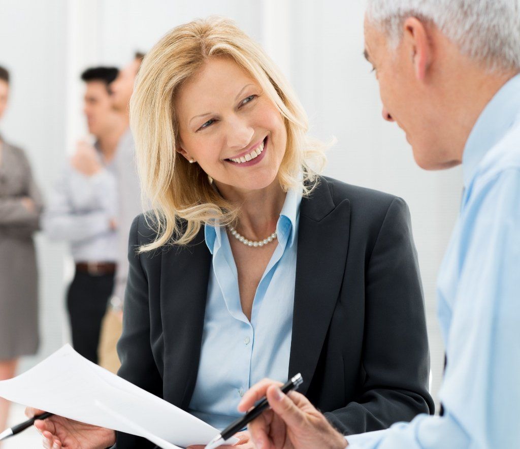 A smiling professional holds a document while collaborating with a colleague in a bright office.