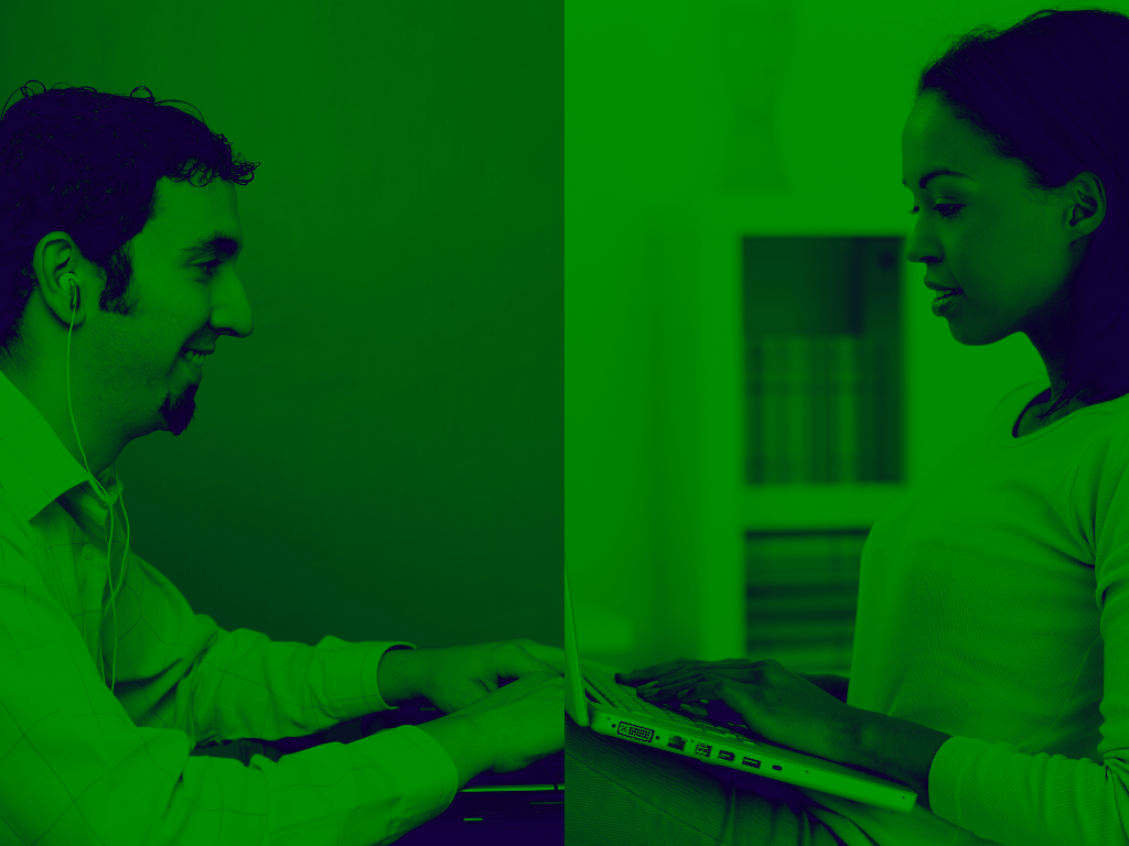 Two people in a green-tinted room work on separate laptops, appearing to be in a professional or office setting.