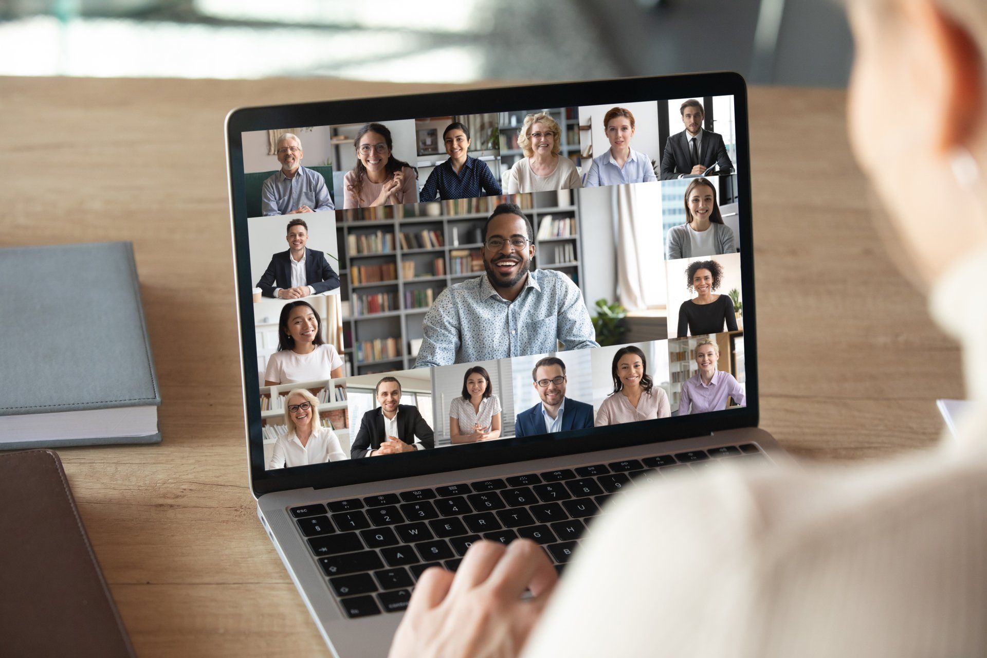 A person views a laptop screen displaying a large group of people during a remote video conference meeting.