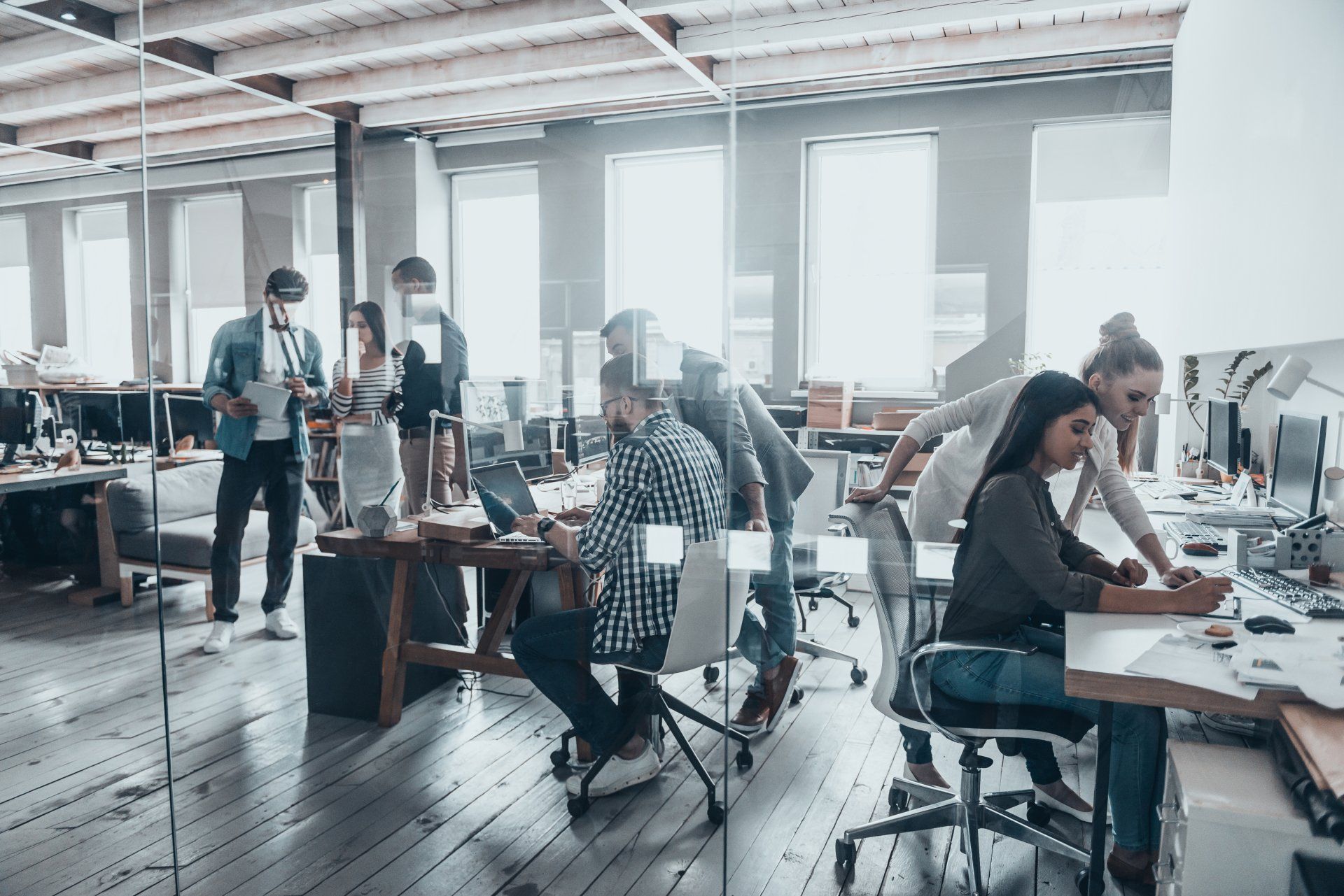 A diverse team works in a bright, open-plan office, with people collaborating at desks and standing in conversation.