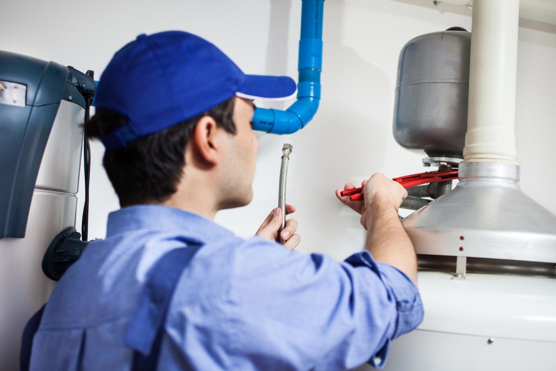 Plumber in blue uniform fixing a water heater with a wrench; indoor setting.