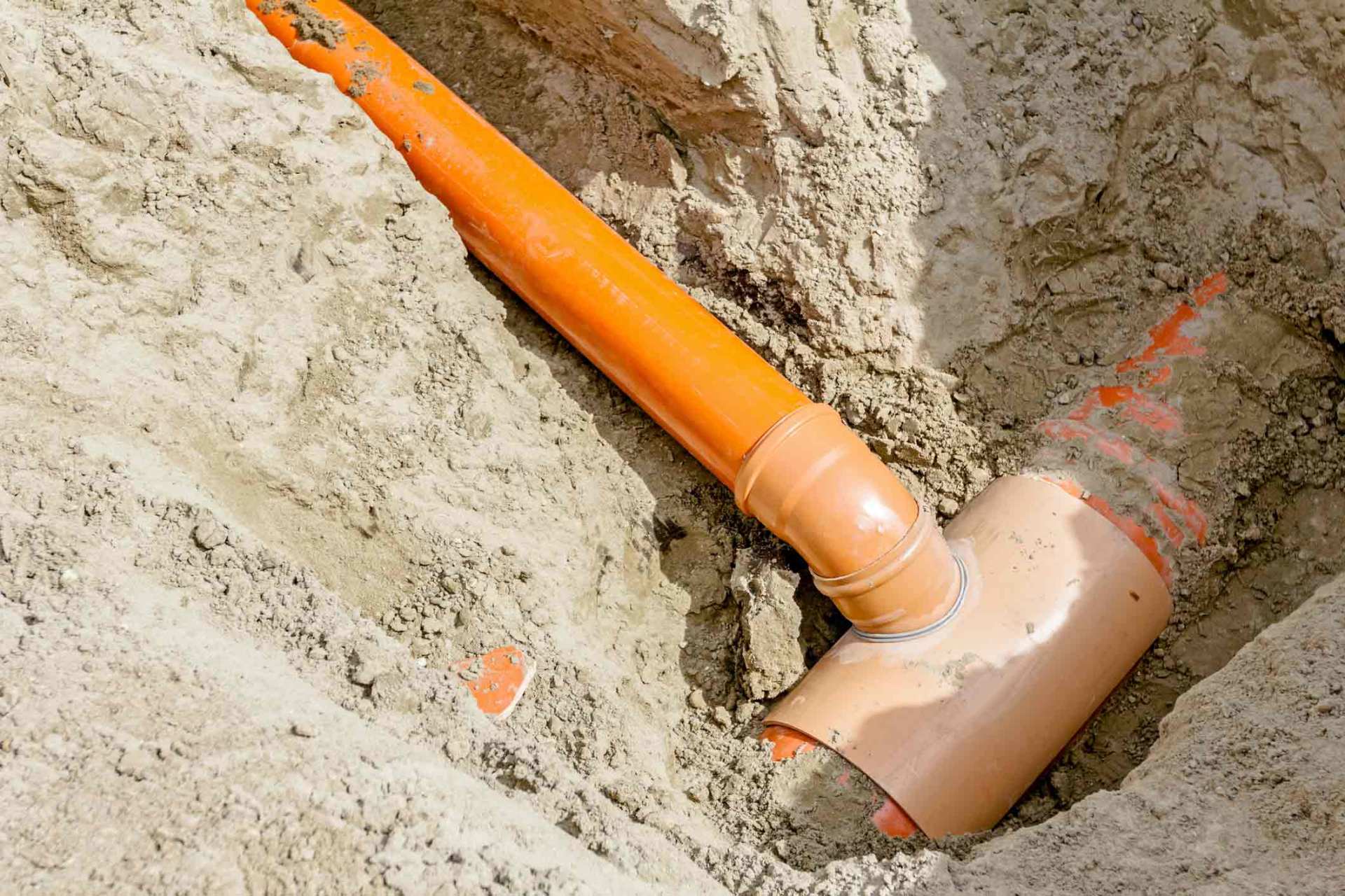 Orange and brown plastic pipes and fittings buried in sand.