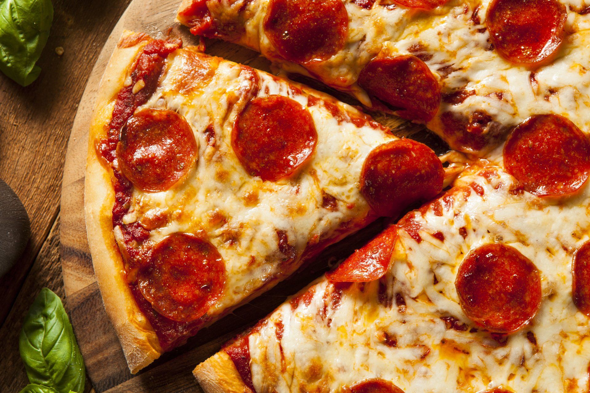 A pepperoni pizza is cut into slices on a wooden cutting board.