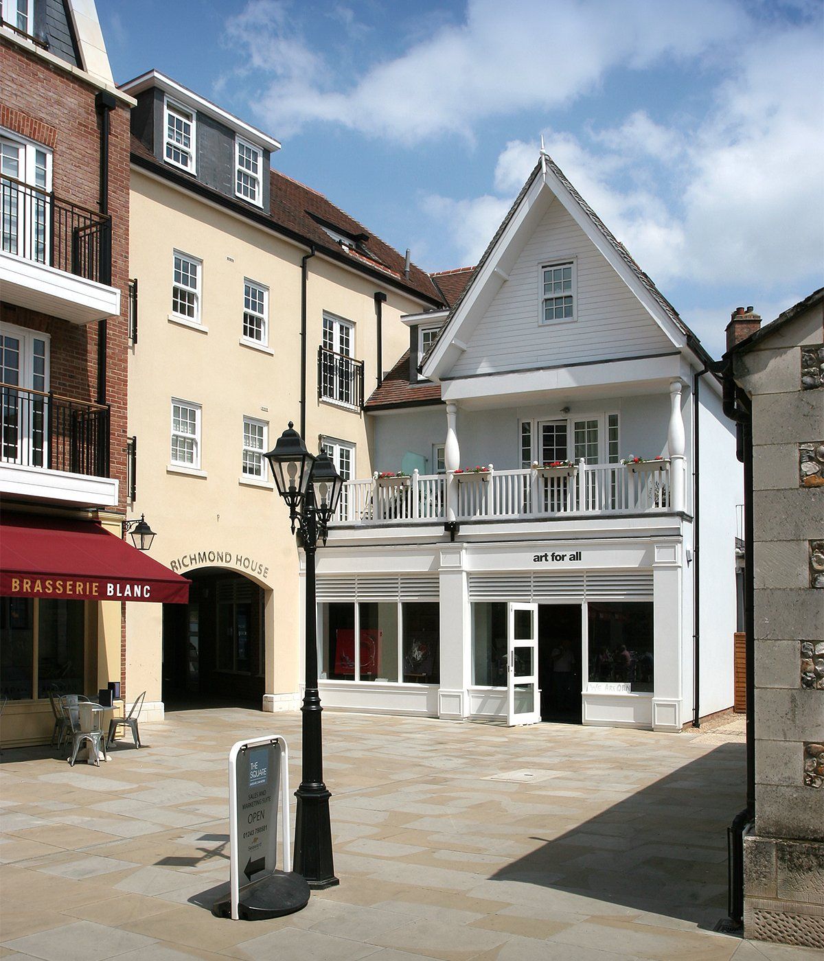 Buildings in a town square: a cream-colored facade with store, brick building, and a white building with a balcony.