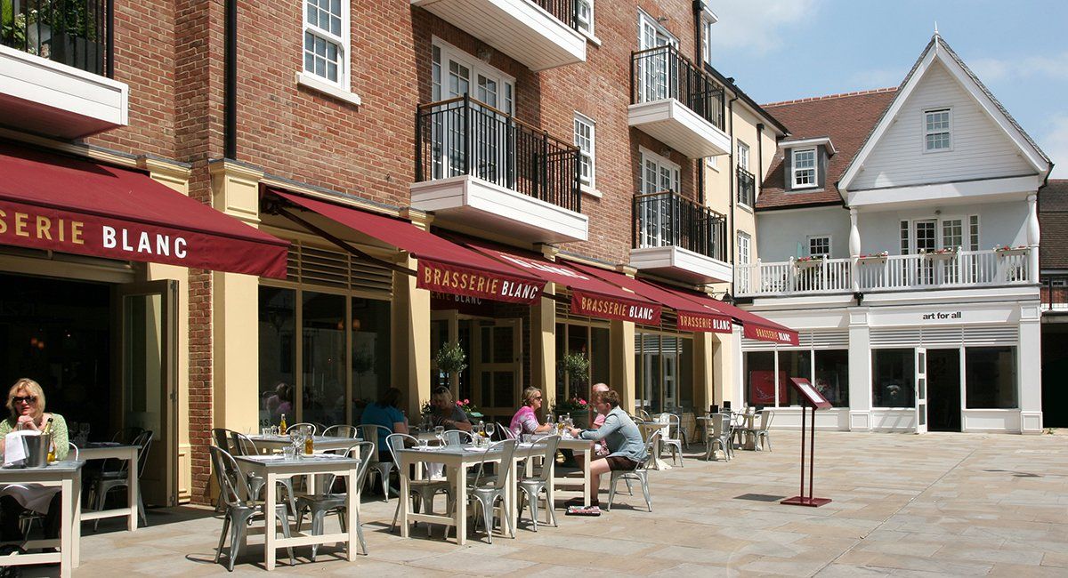 Outdoor dining area with red awnings, tables, and people. Brick and cream-colored buildings.