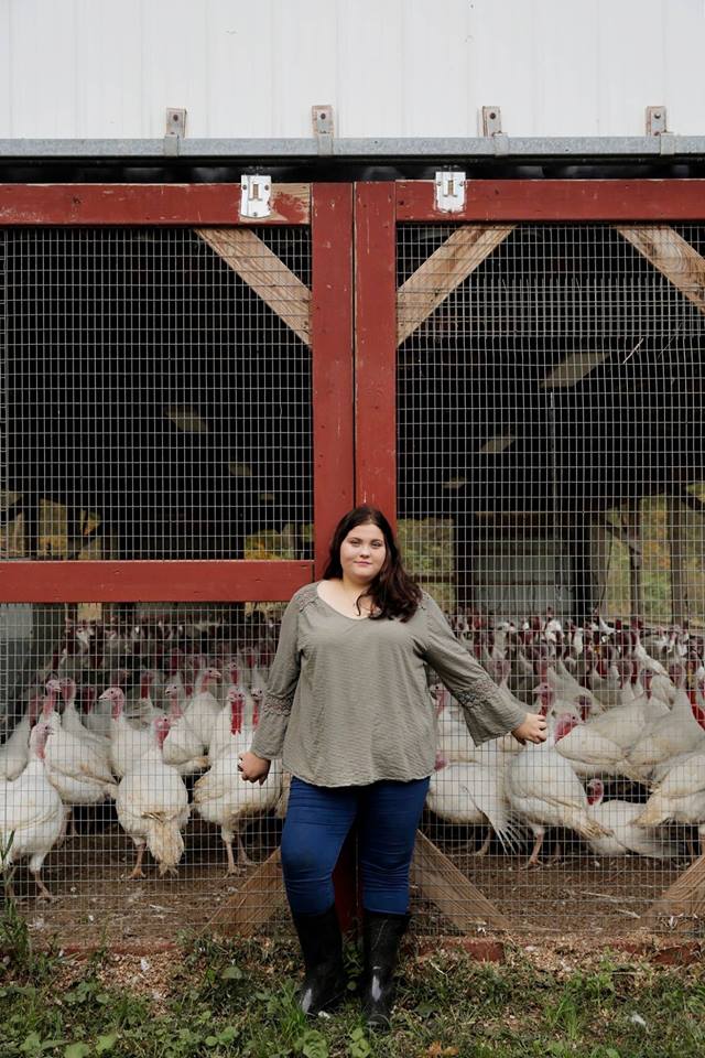 A woman is standing in front of a fence surrounded by turkeys.