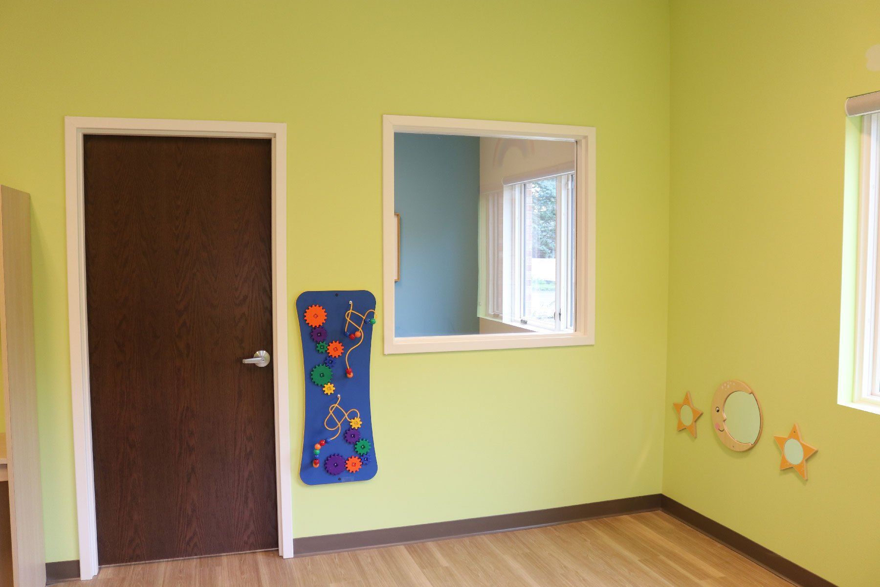 A room with green walls , a wooden floor , a door and a window.