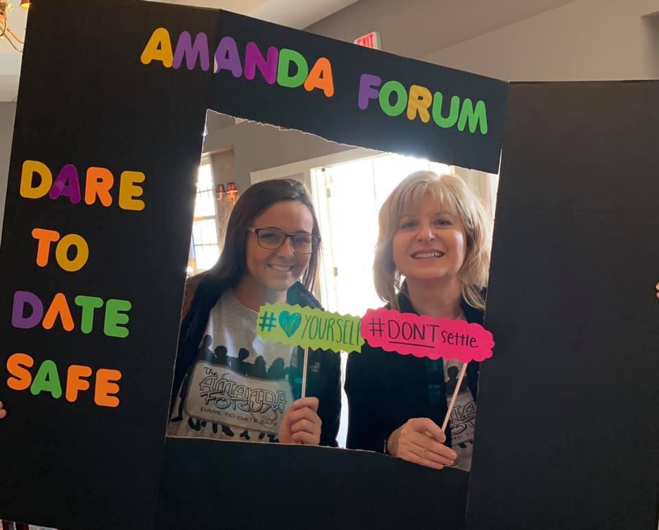Two women are posing for a picture in front of a sign that says dare to date safe.