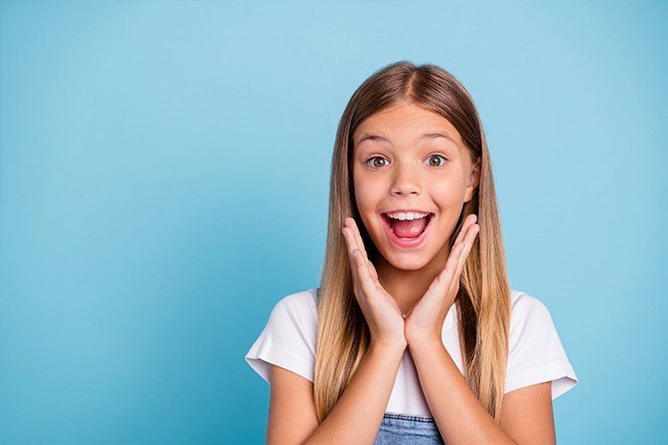 A young girl with a surprised look on her face is holding her hands to her face.