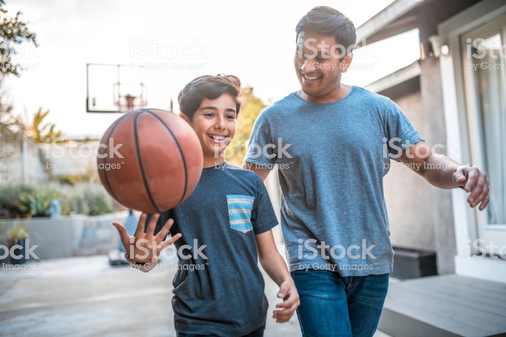 A father and son are playing basketball together on a court.