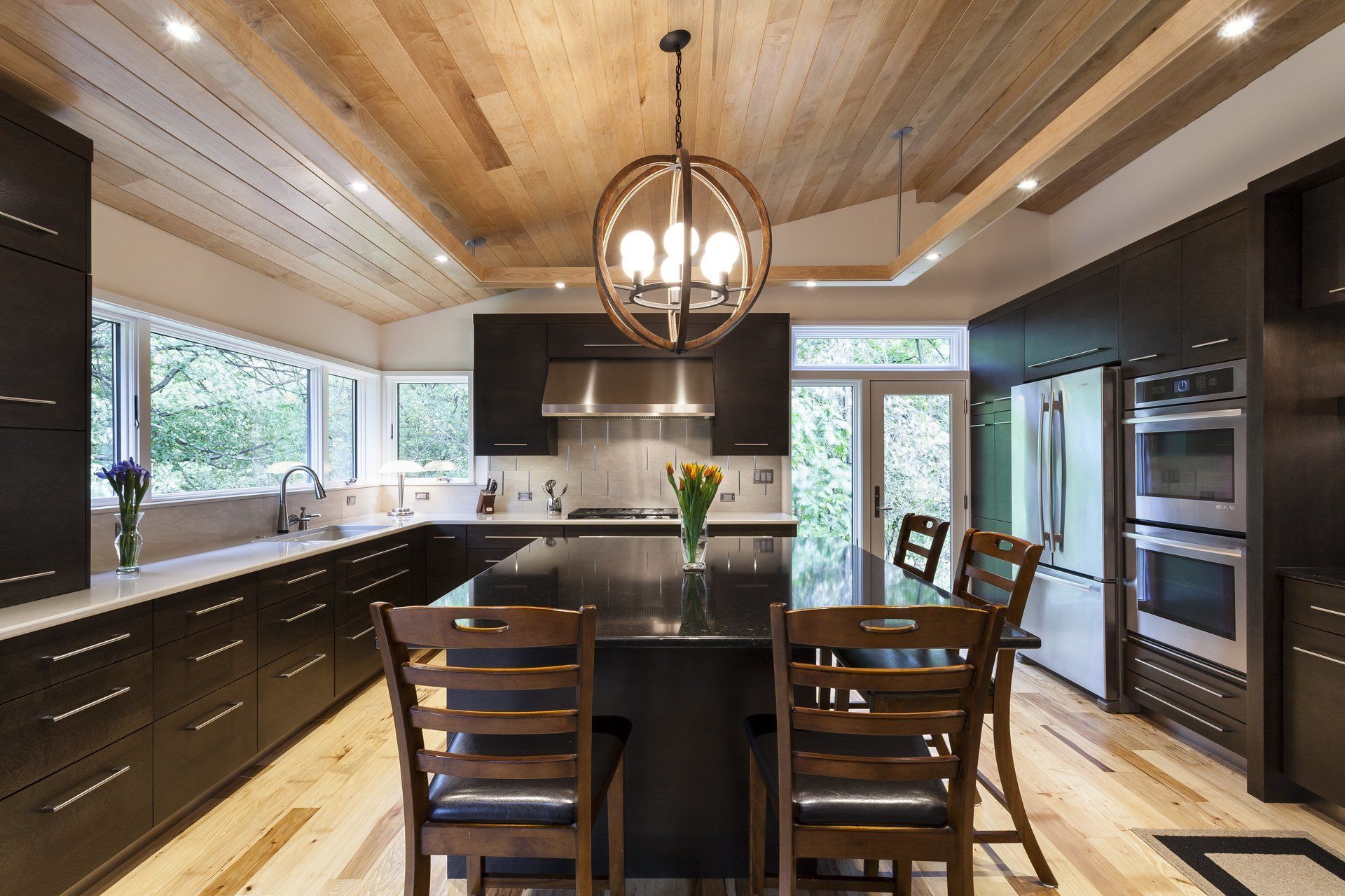 Modern kitchen with dark cabinets, wood ceiling, island seating, pendant light, and large windows
