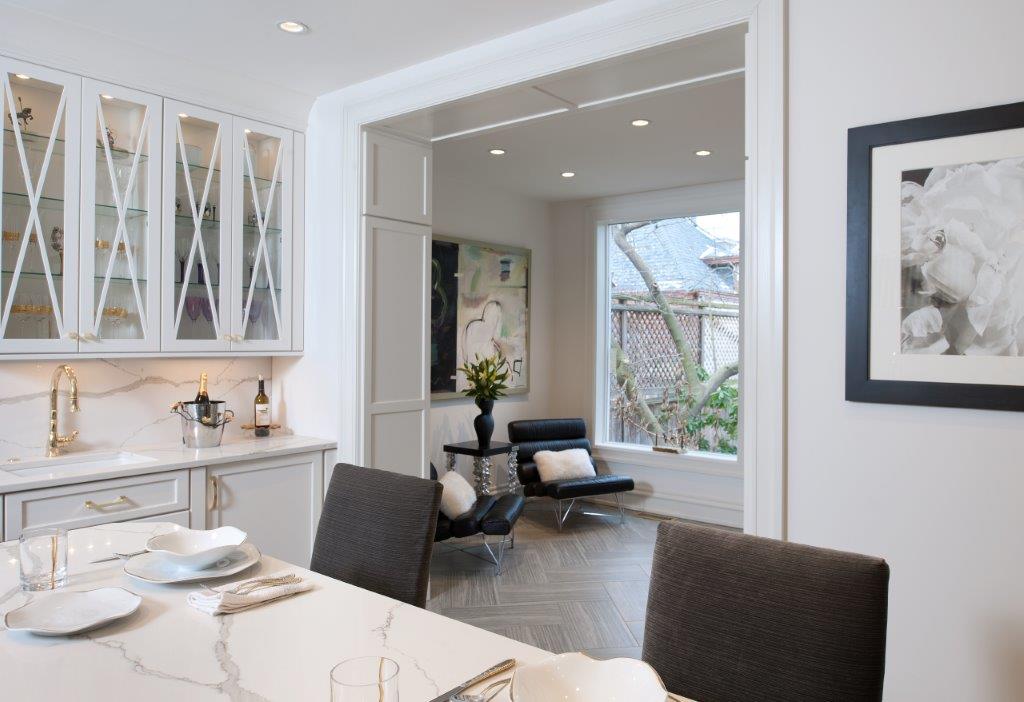 Bright modern dining room opening to a cozy living area and outdoor view, with white cabinetry and dark chairs