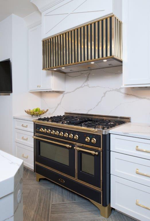 Modern white kitchen with a black and gold range, marble backsplash, and sleek cabinets