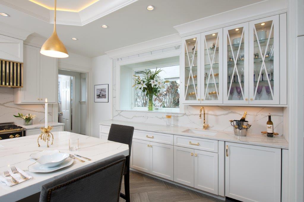 Bright white modern kitchen with island, glass cabinets, gold accents, and a large window by the dining table