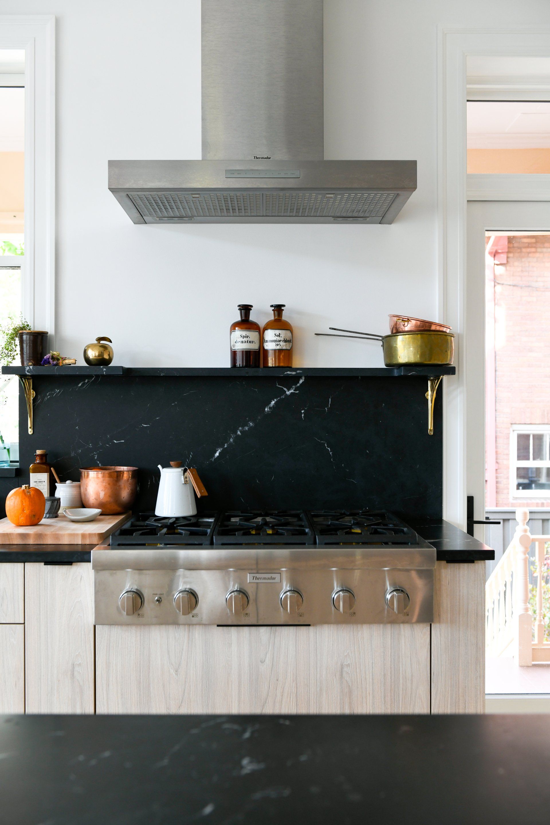 Modern kitchen with stainless steel range hood, black backsplash, and gas stove below a windowed wall