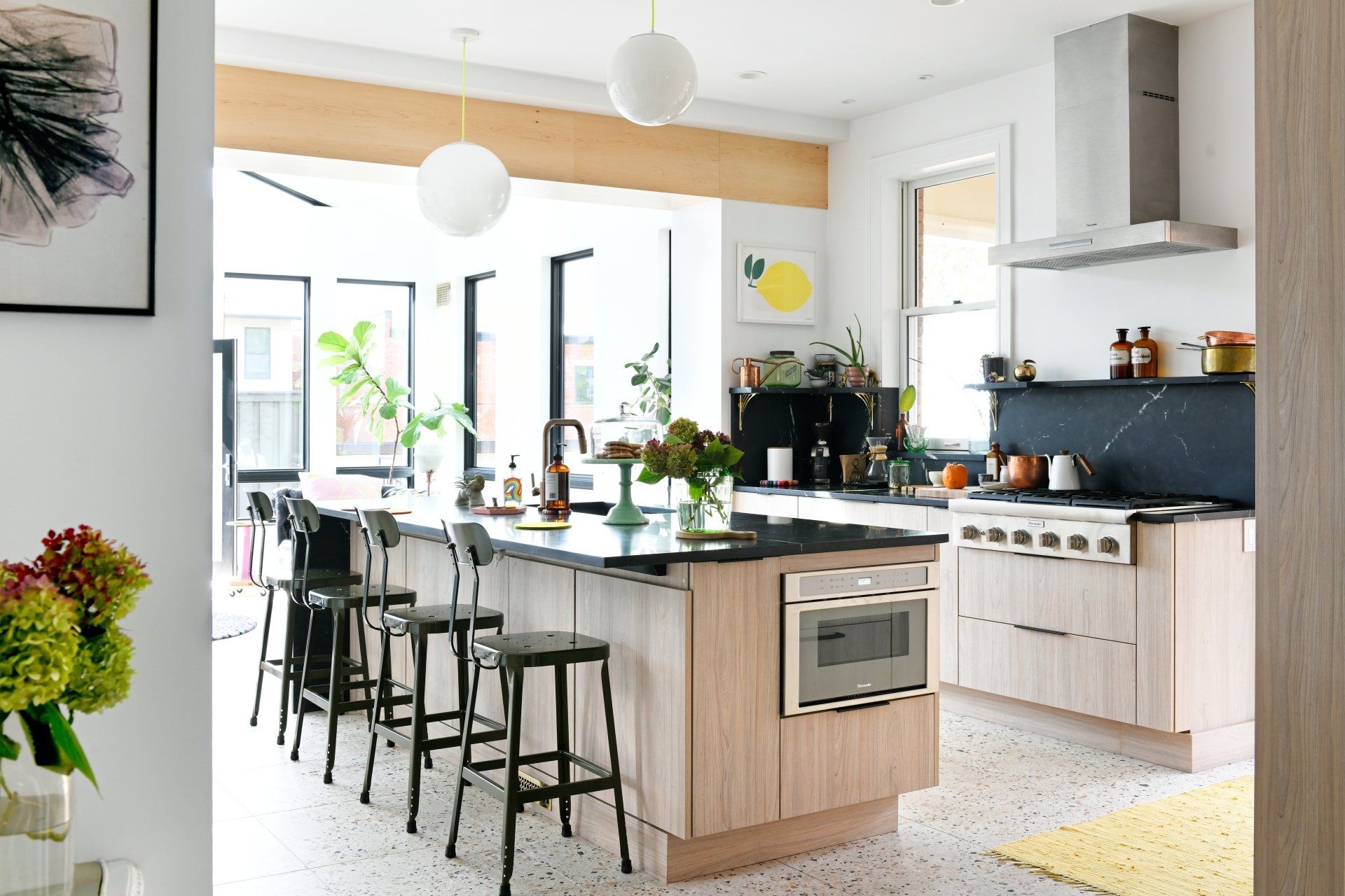 Bright modern kitchen with island, bar stools, white cabinets, and large windows in natural light