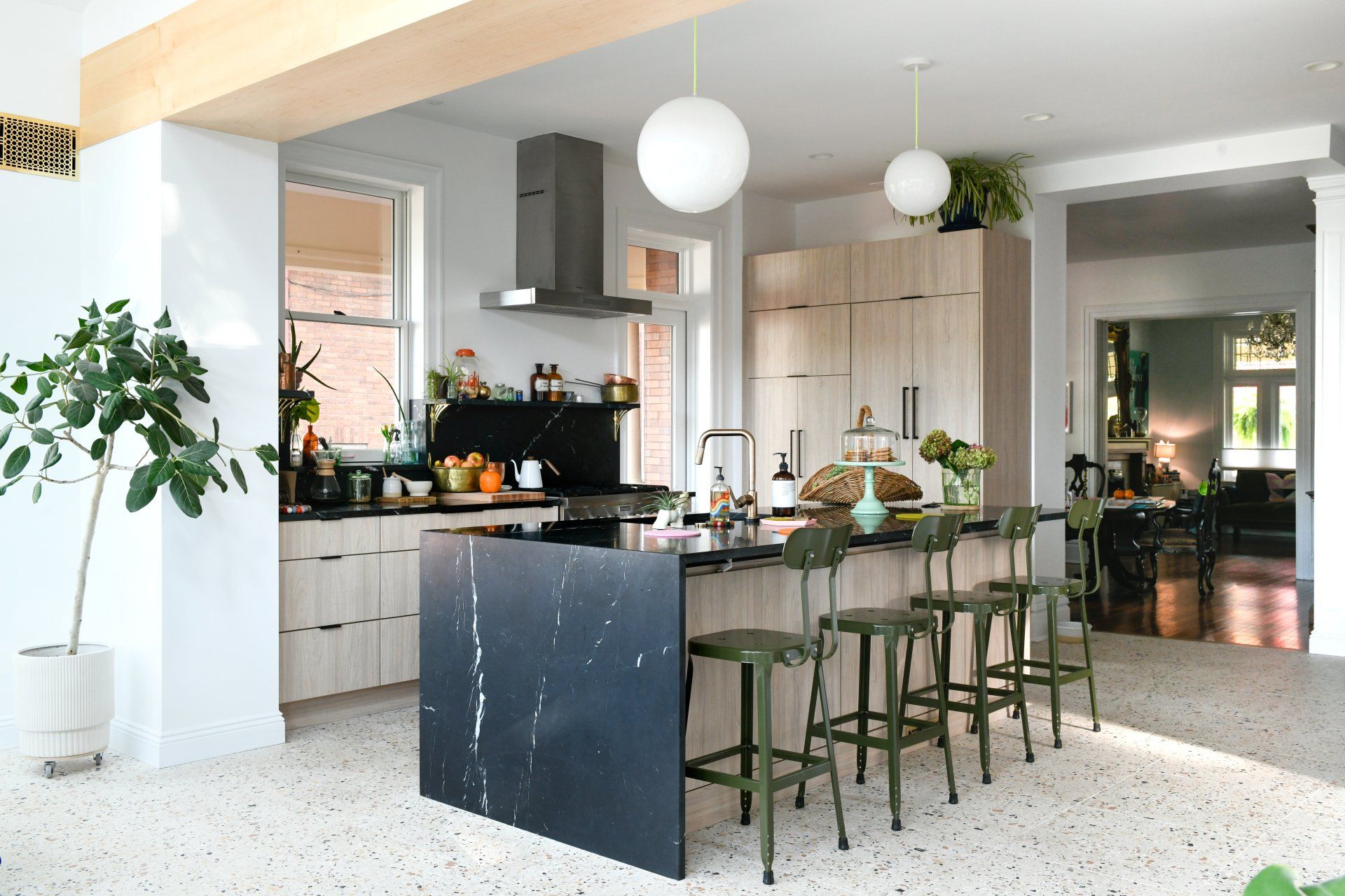Bright modern kitchen with black island, green stools, white cabinets, and hanging globe lights