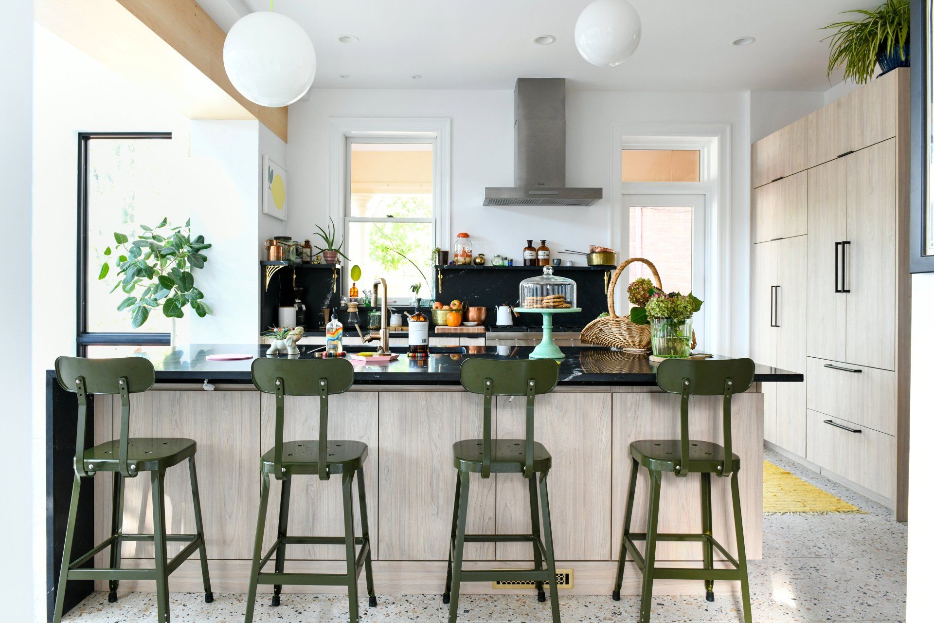 Modern kitchen with white island, green bar stools, plants, and stainless steel range hood