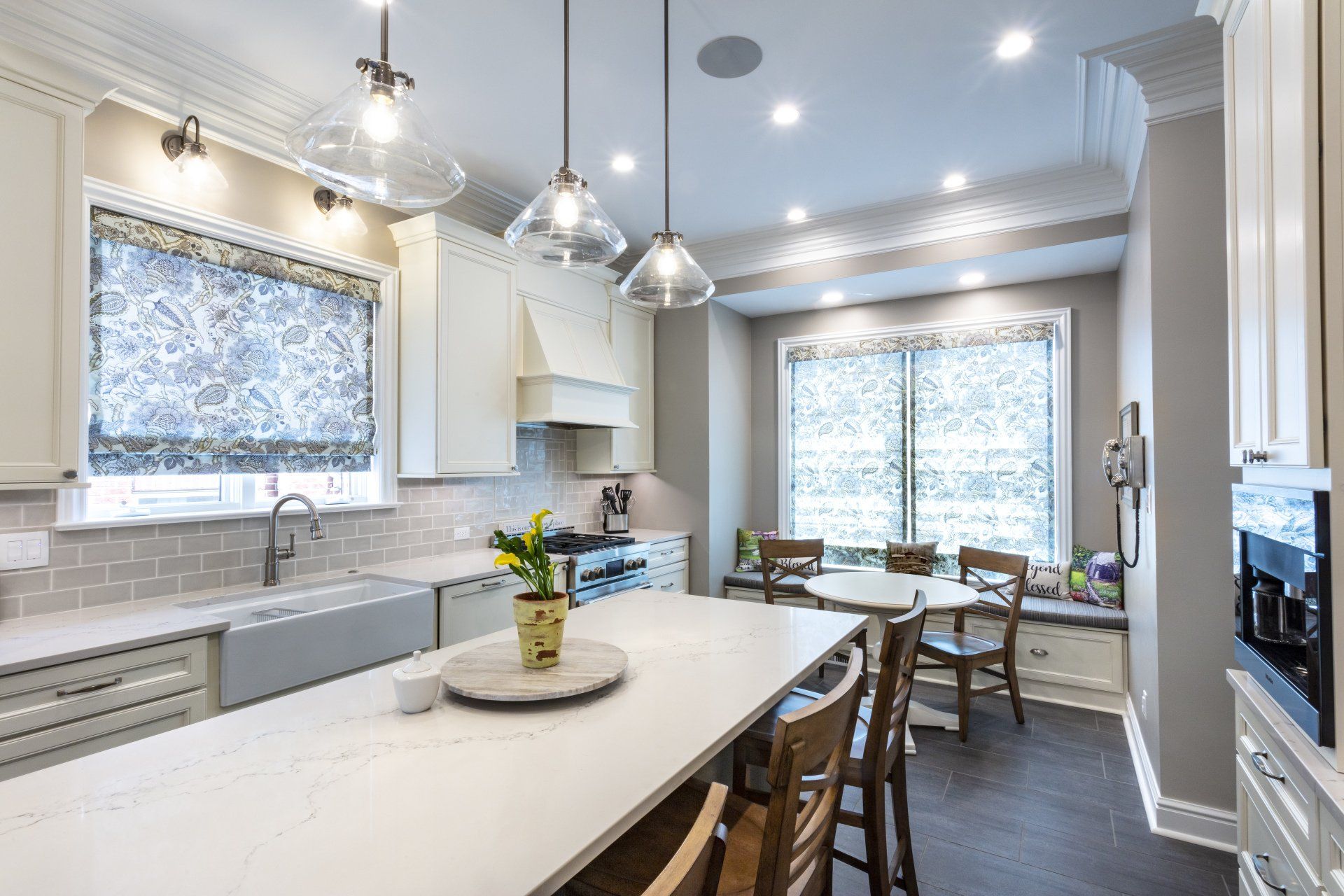 Bright white kitchen with island, pendant lights, gray tile, and dining nook by large windows