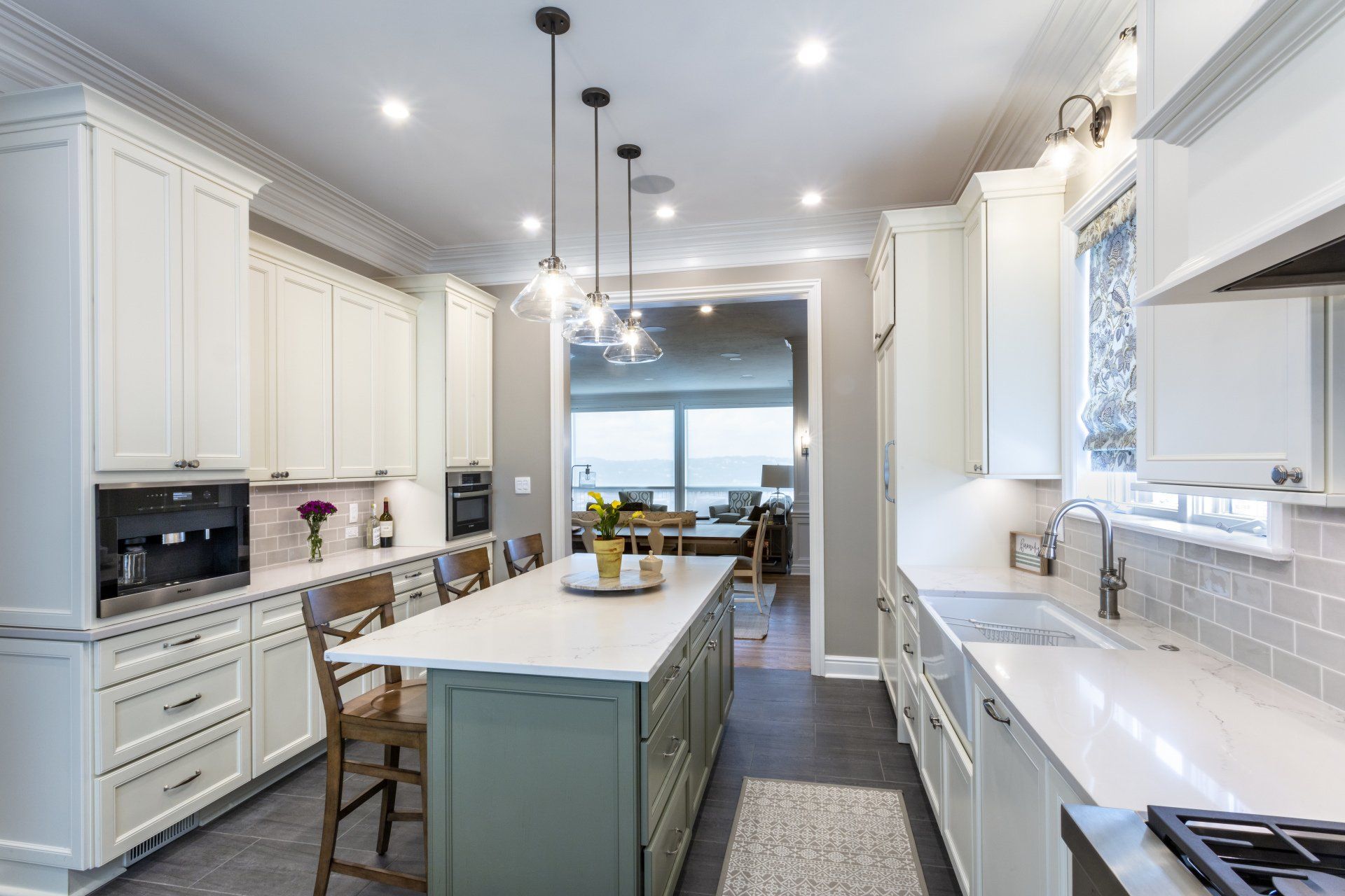 Bright white kitchen with a large island, pendant lights, and a windowed dining area.