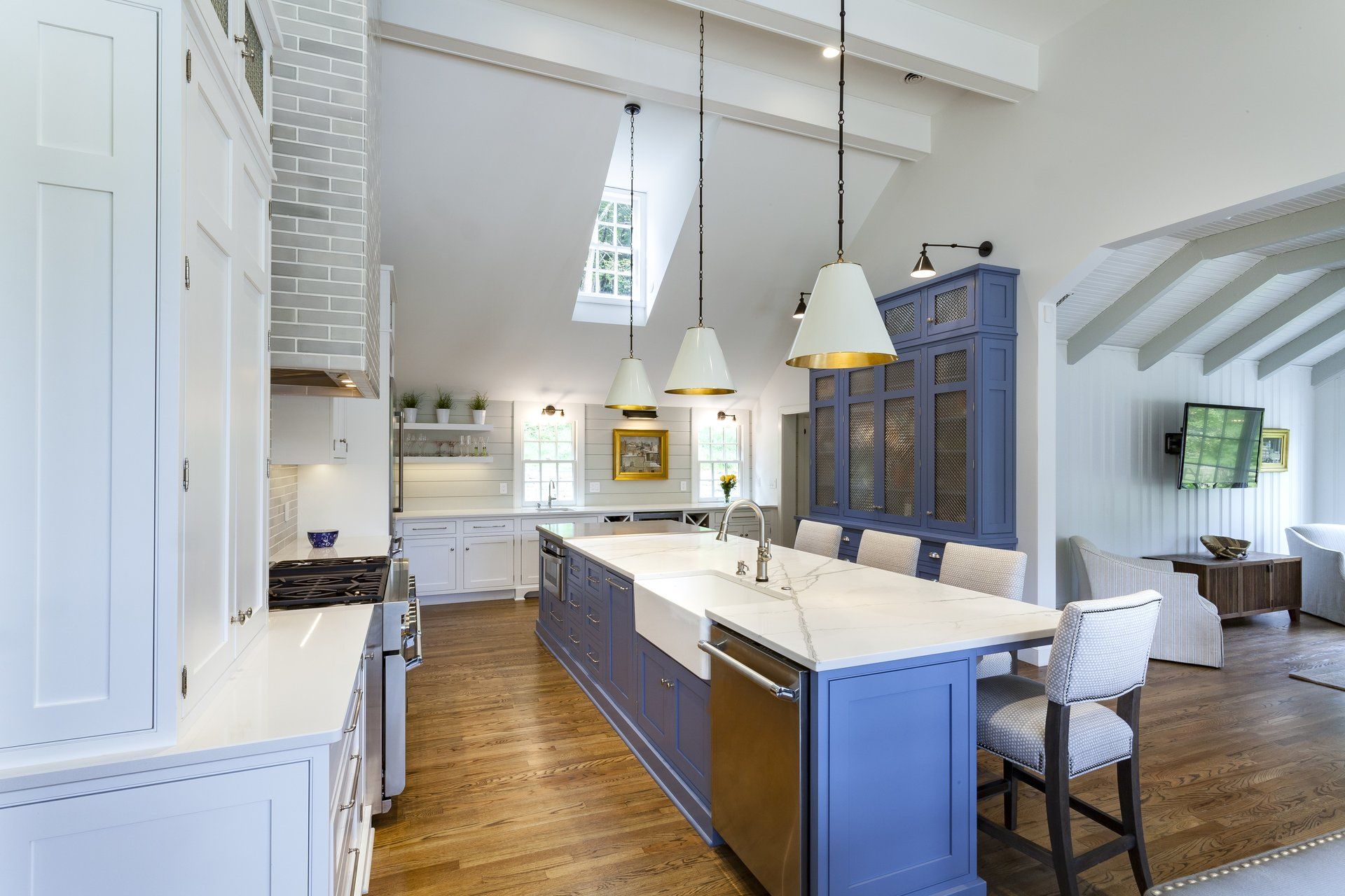 Bright modern kitchen with white cabinets, blue island, pendant lights, and wood floors