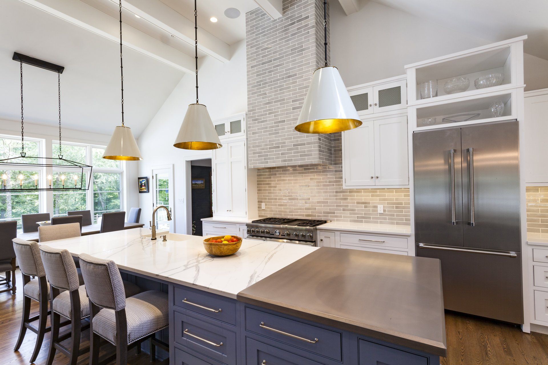 Modern kitchen with white island, pendant lights, marble backsplash, and stainless-steel refrigerator