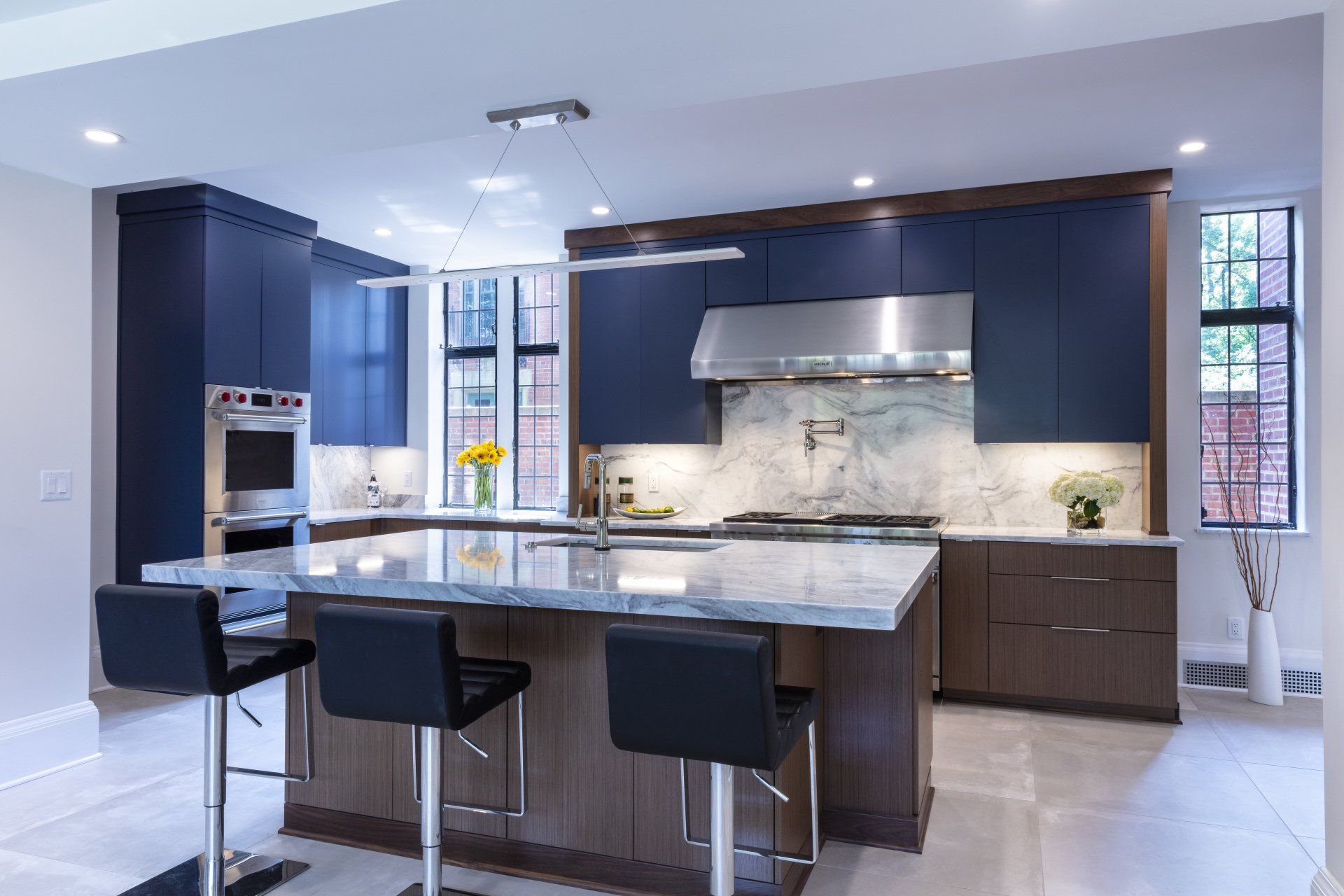 Modern kitchen with navy cabinets, marble island, stainless appliances, and four black bar stools