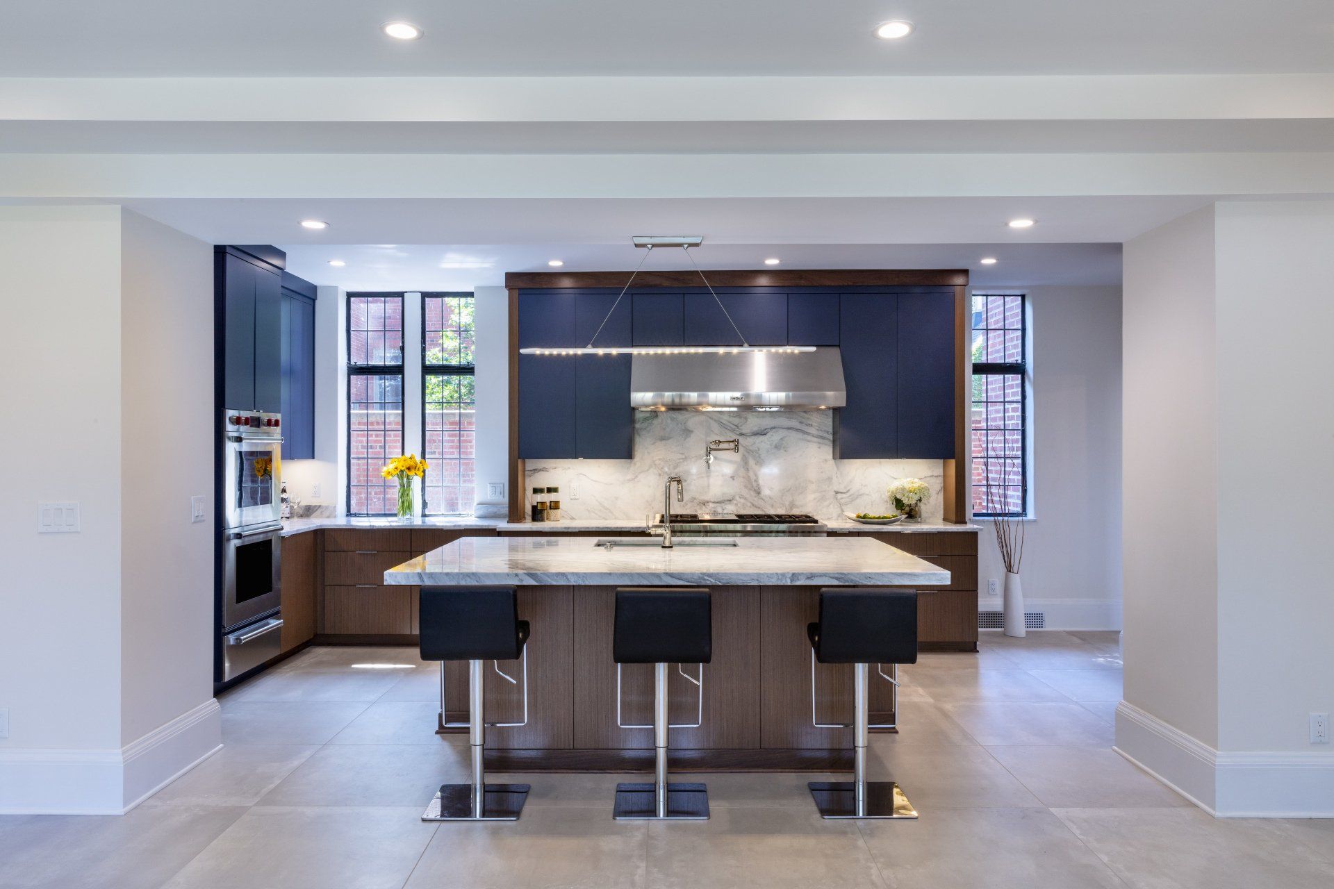 Modern kitchen with large island, dark cabinets, marble backsplash, and recessed ceiling lights