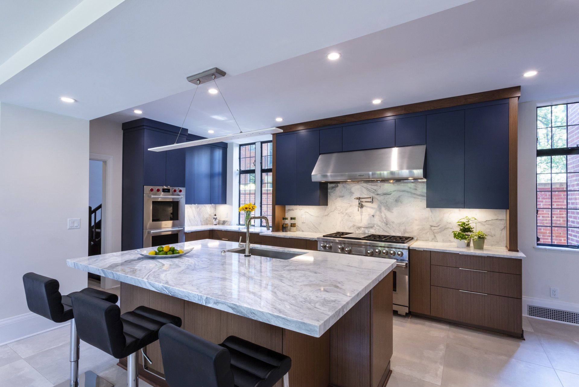 Modern kitchen with large marble island, dark cabinets, and stainless steel range hood