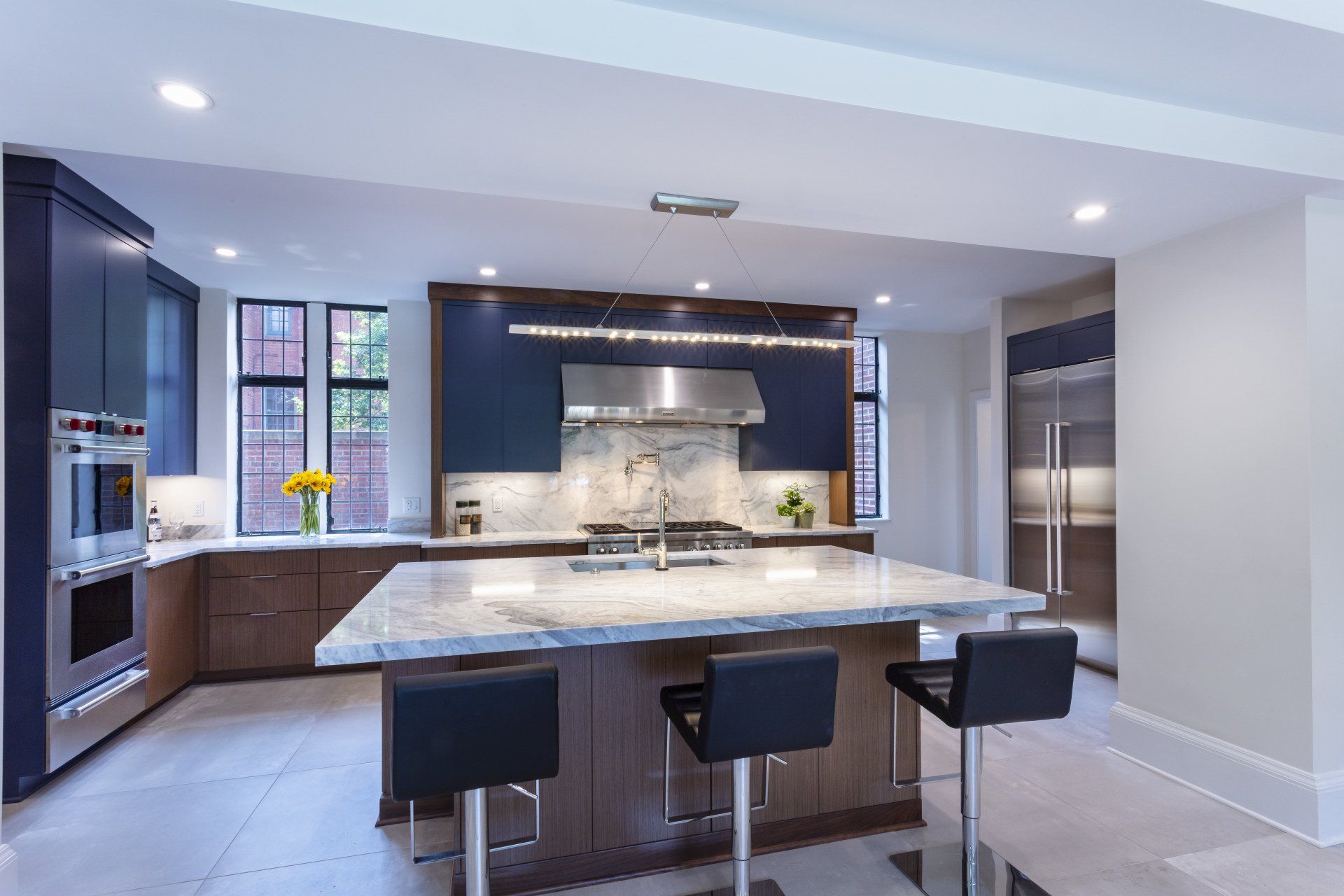 Modern kitchen with large island, three stools, stainless appliances, and dark cabinetry