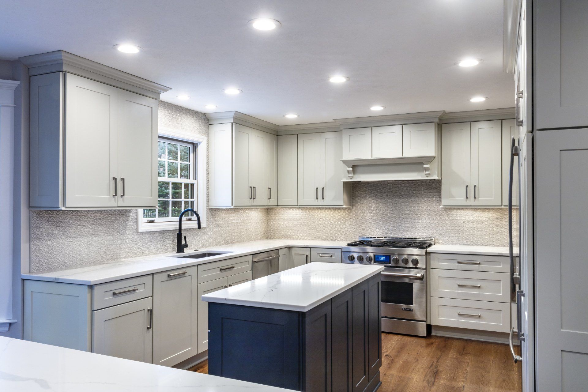Bright modern kitchen with white cabinets, gray backsplash, island, and stainless steel appliances.