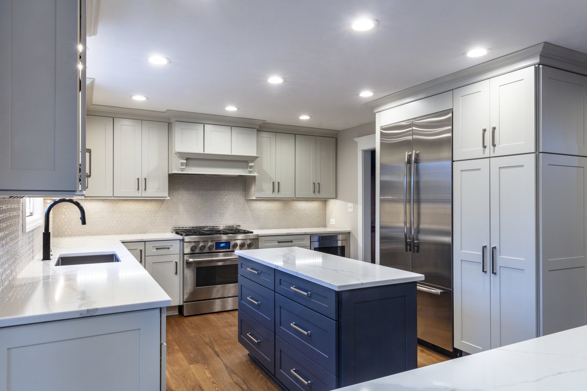 Modern kitchen with gray cabinets, stainless steel appliances, white countertops, and a navy island