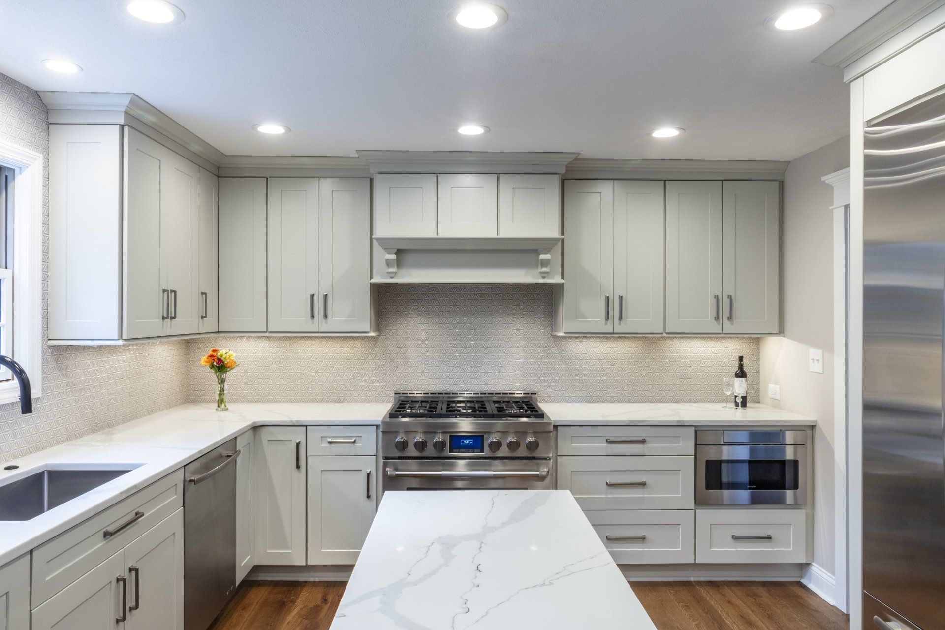 Bright modern kitchen with white cabinets, marble island, stainless-steel appliances, and recessed lighting
