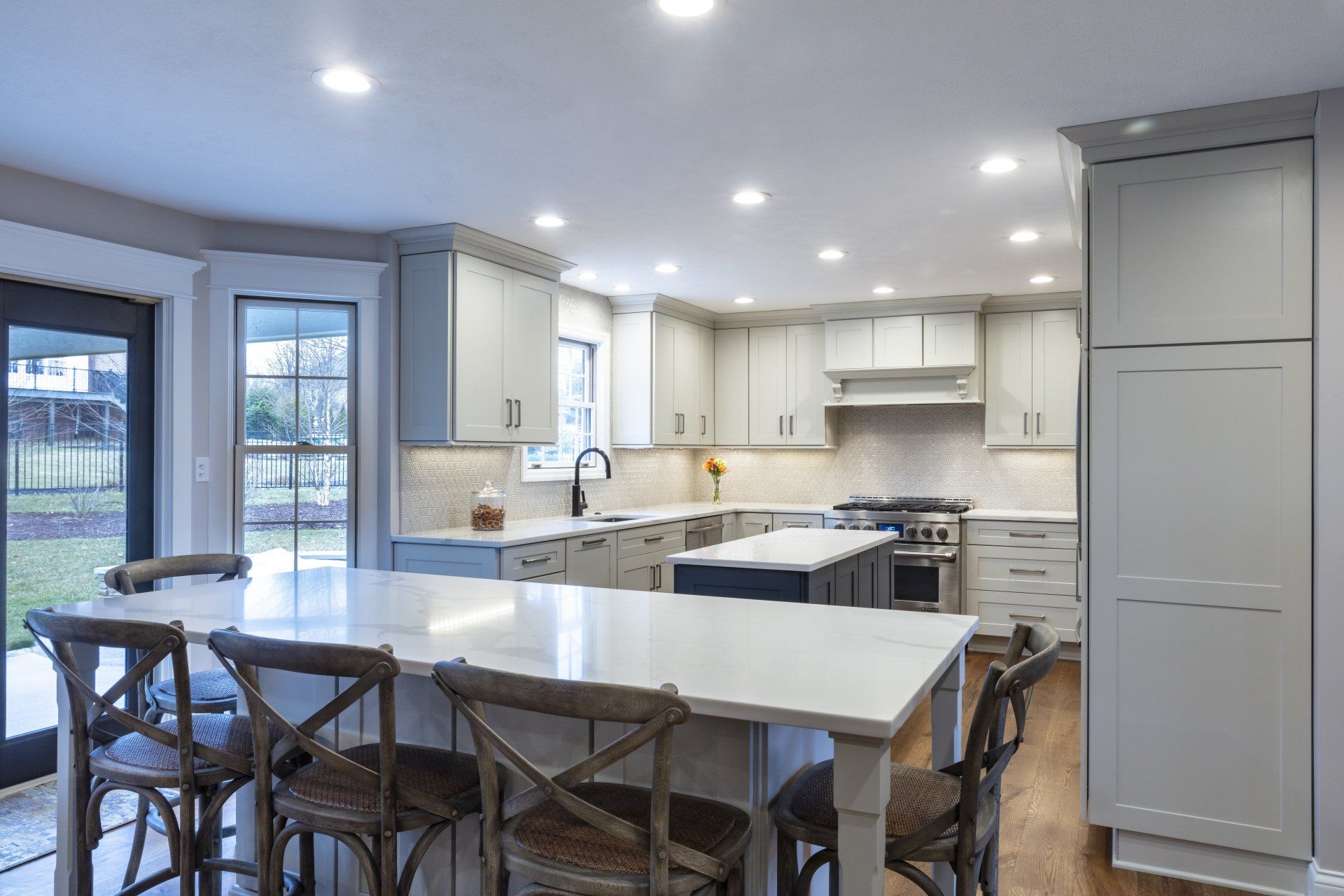 Bright modern kitchen with white island, gray cabinets, bar stools, and large windows