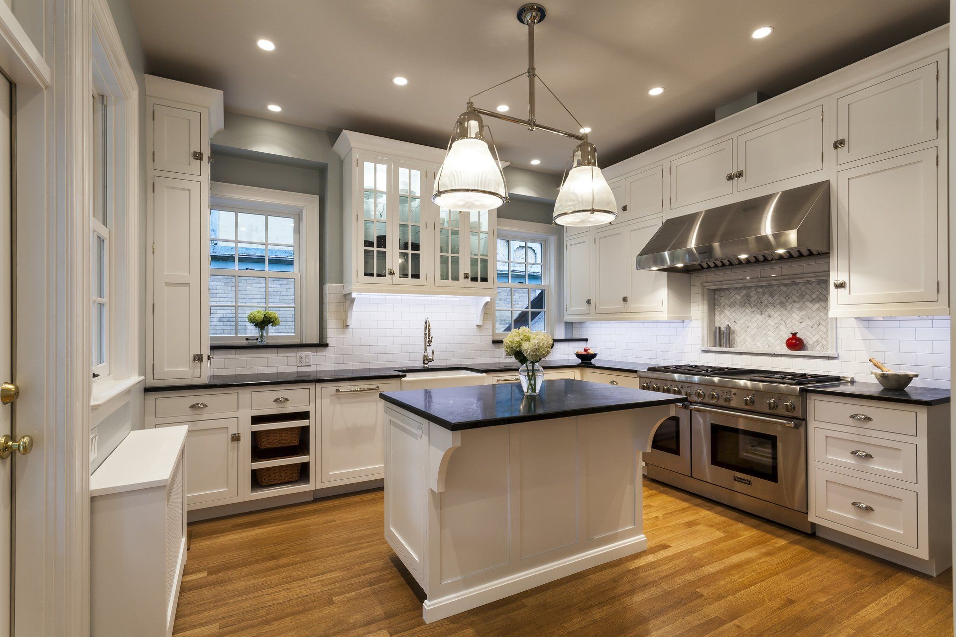 Modern white kitchen with island, stainless steel appliances, wood floors, and pendant lights