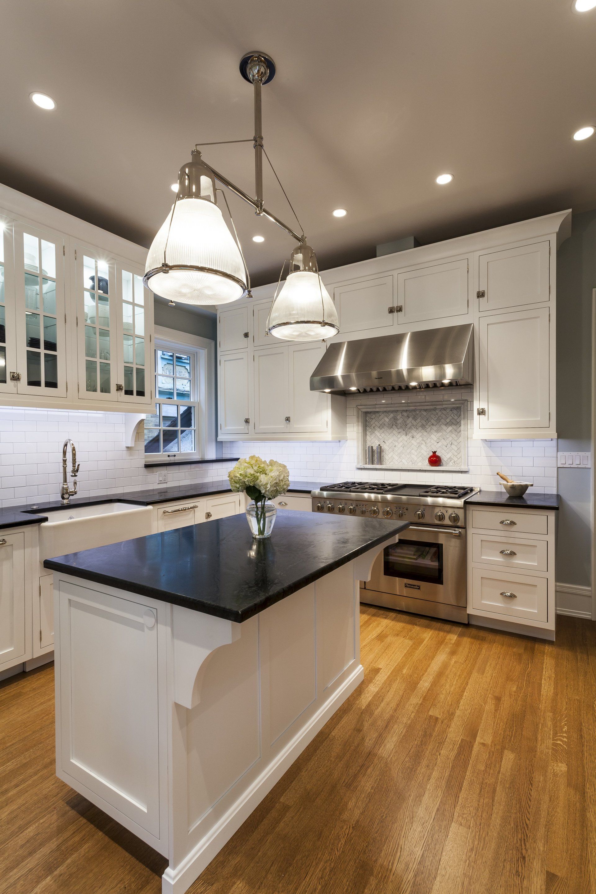 Bright modern kitchen with white cabinets, black island, pendant lights, and hardwood floors