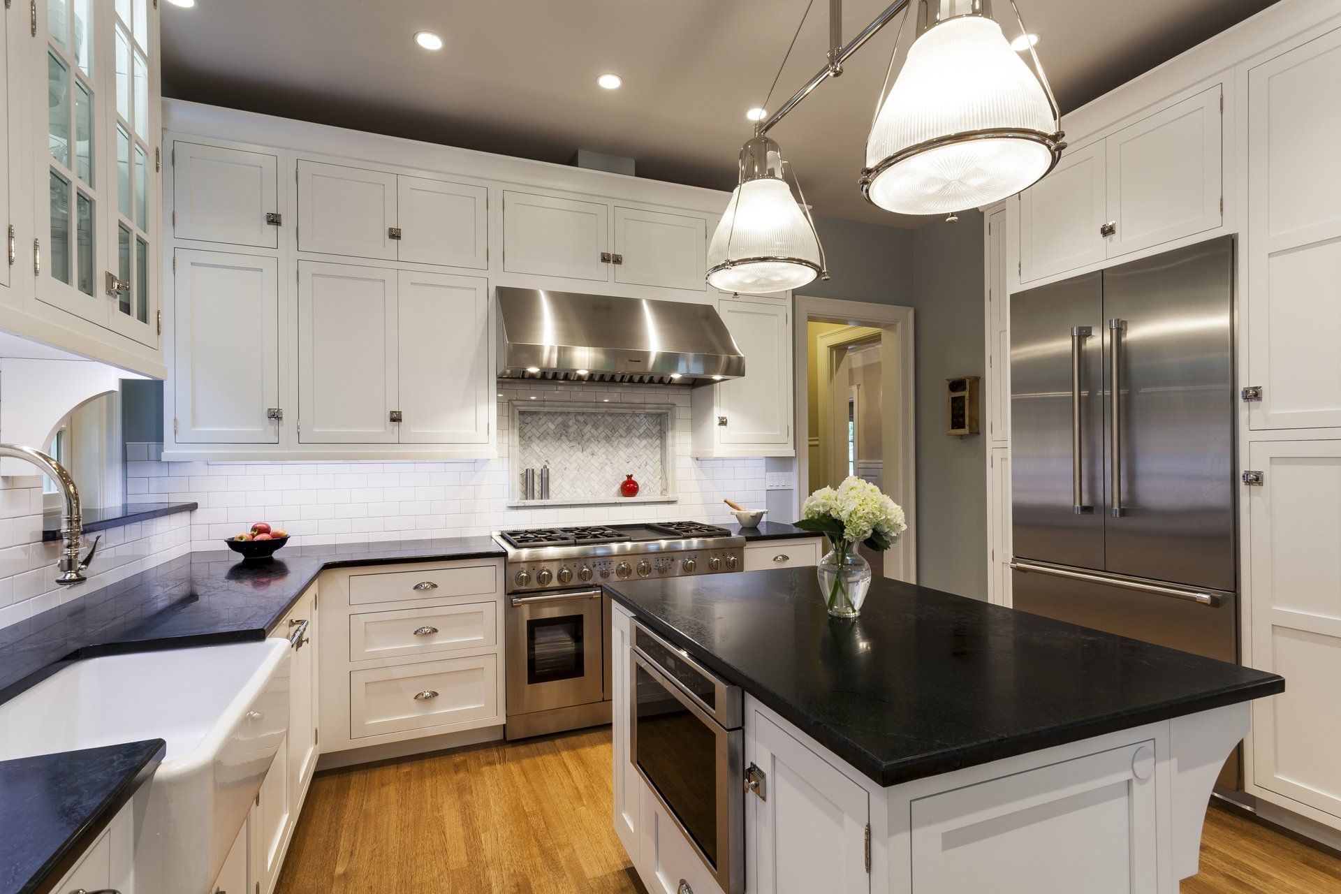 A kitchen with white cabinets , black counter tops , stainless steel appliances and a large island.