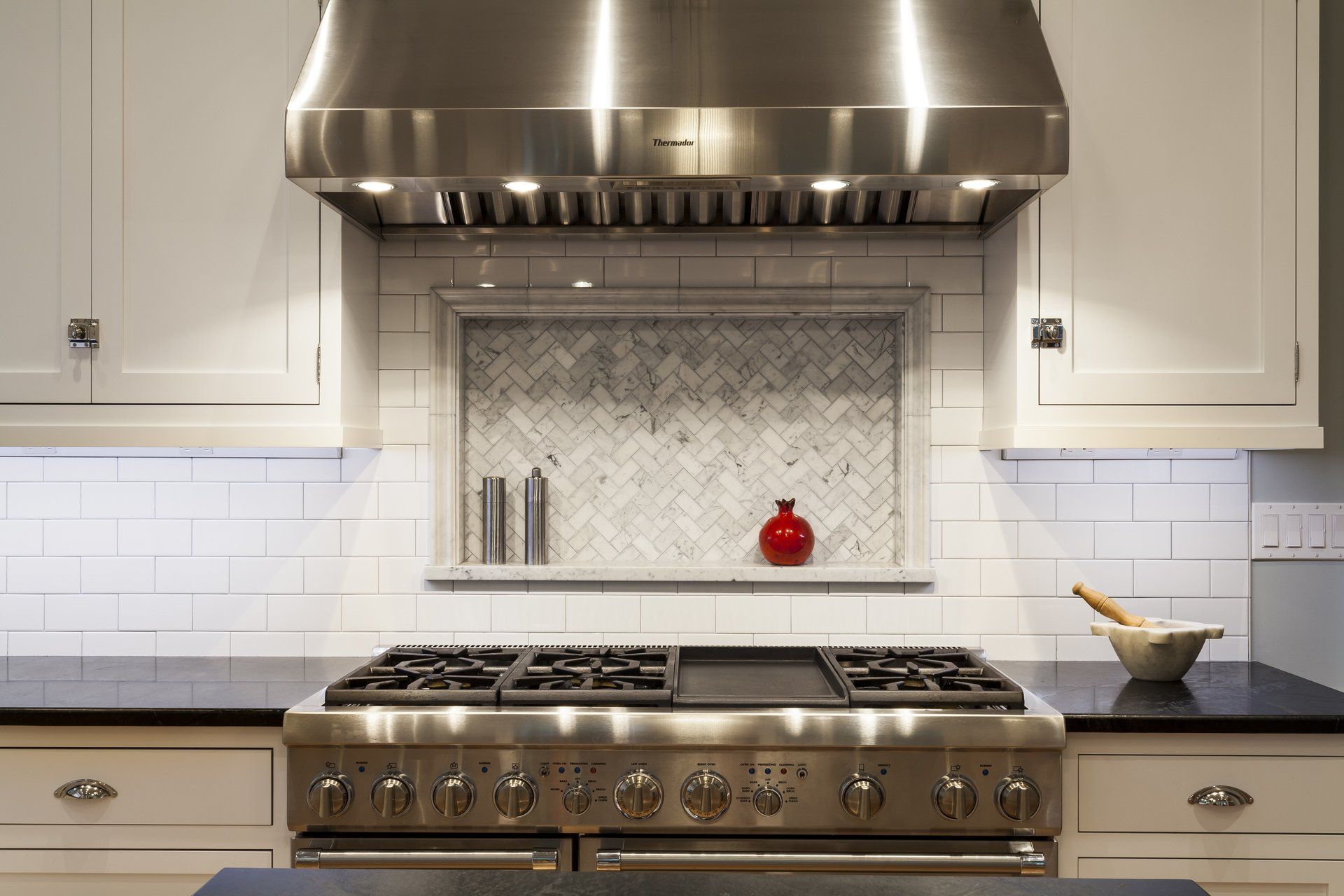 Modern kitchen with stainless steel range, hood, white cabinets, and tiled backsplash