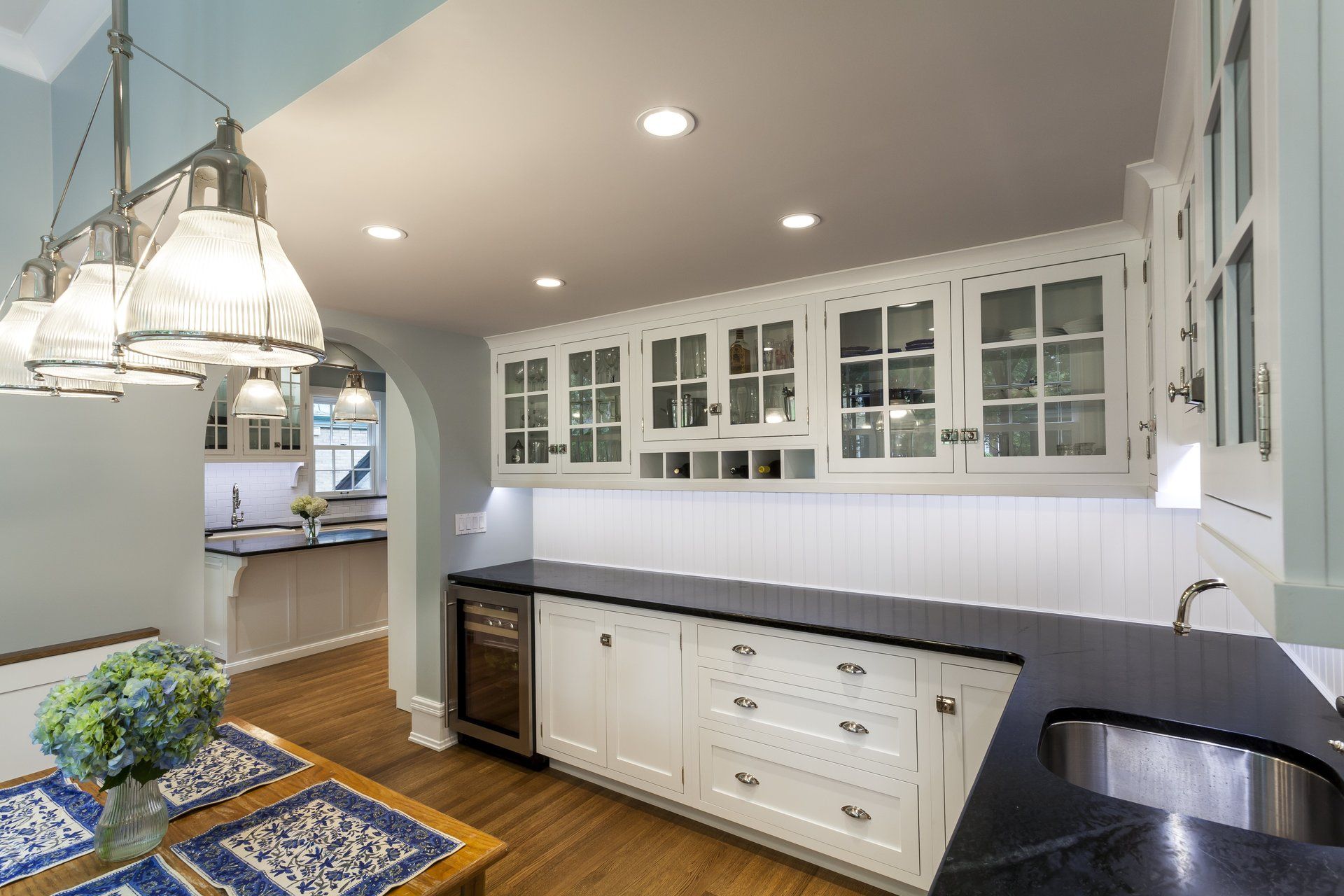 Bright kitchen with white cabinets, black countertops, pendant lights, and a small table with flowers.