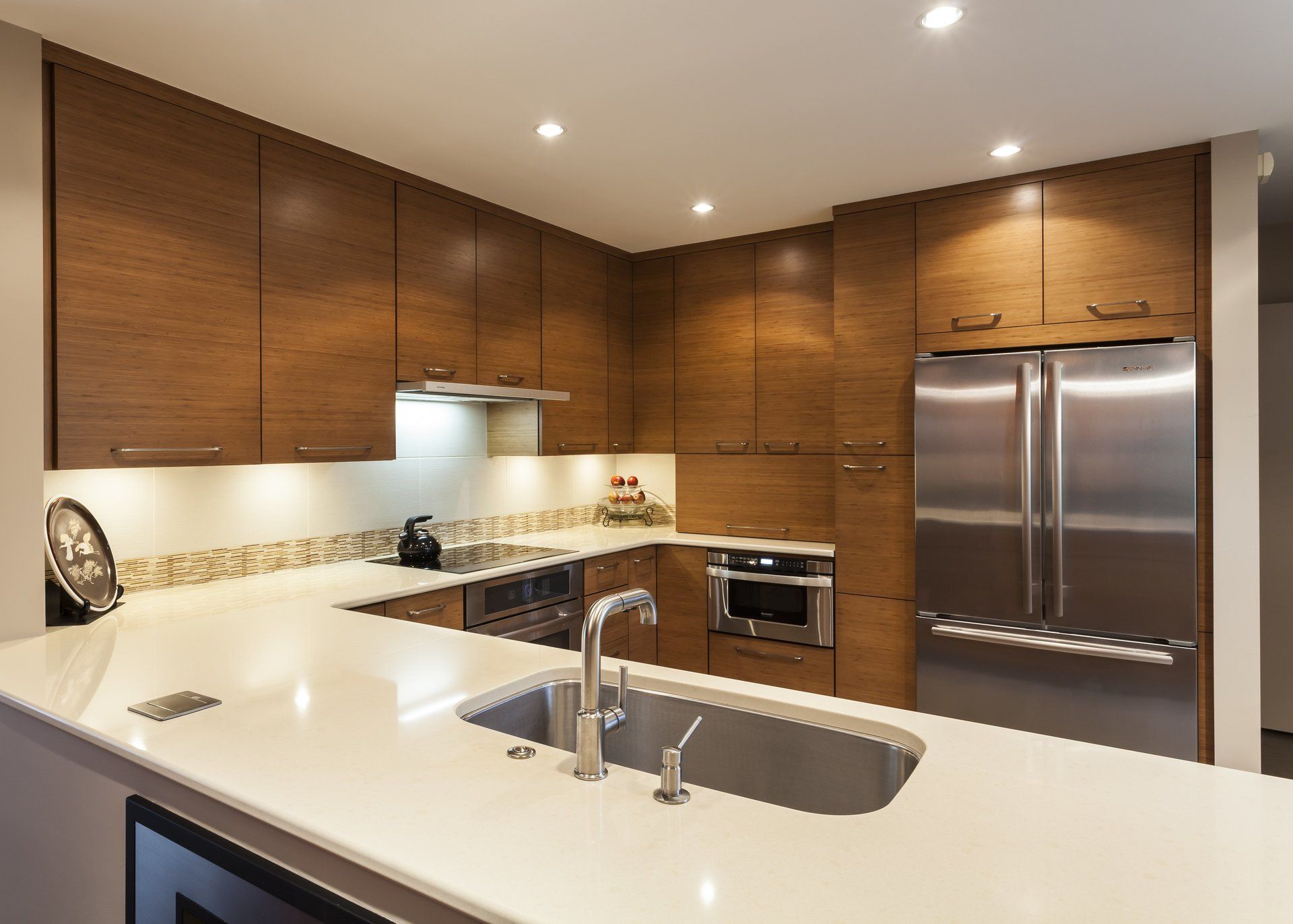 Modern kitchen with dark wood cabinets, white countertops, and stainless steel appliances and sink.