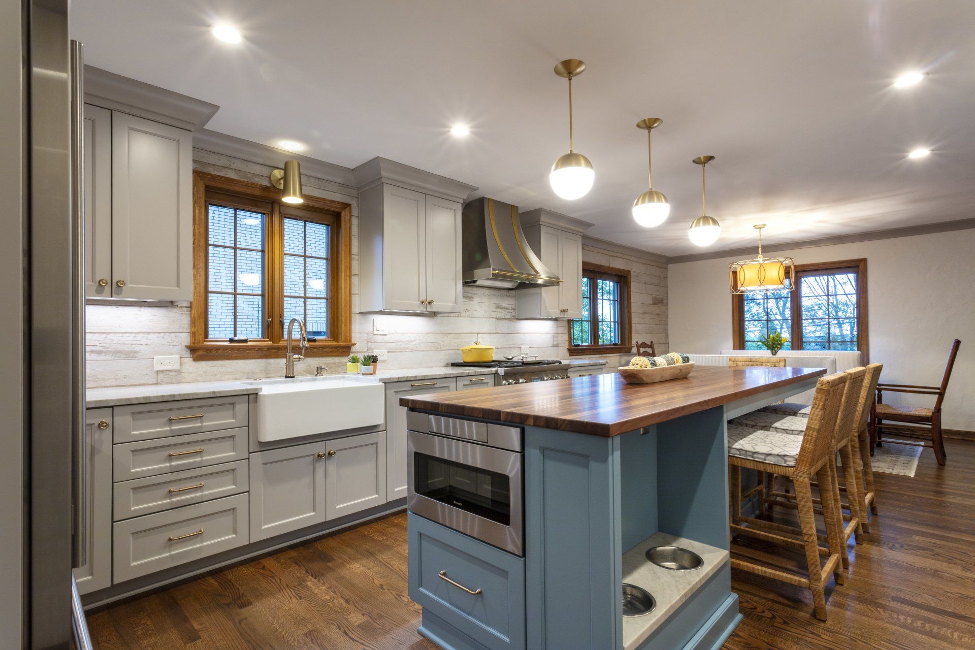 Bright modern kitchen with white cabinets, blue island, wooden floors, and bar stools