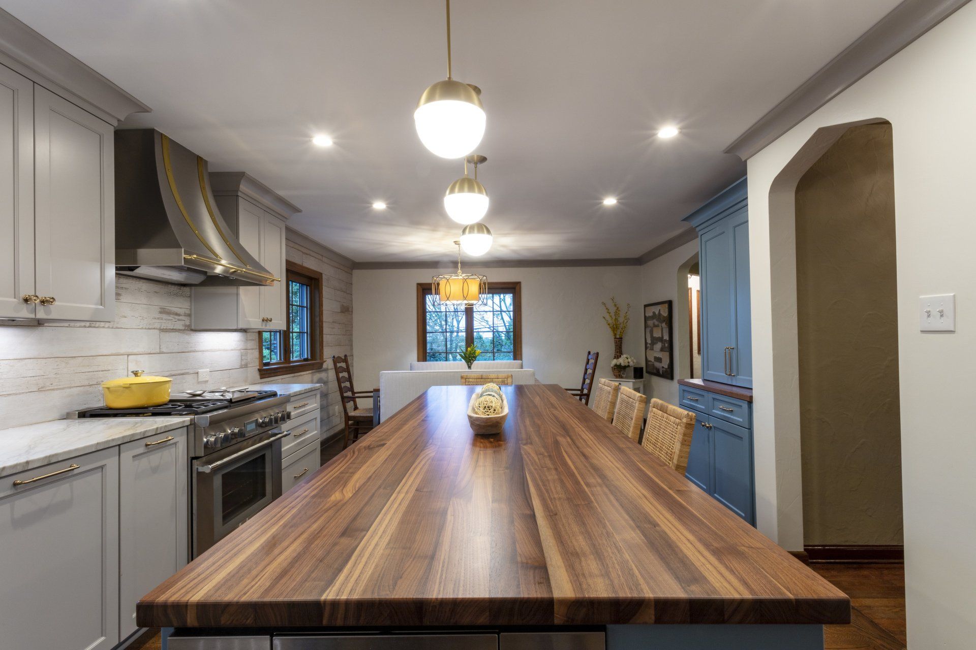 Modern kitchen with a long wooden island, gray cabinets, pendant lights, and a window at the far end.
