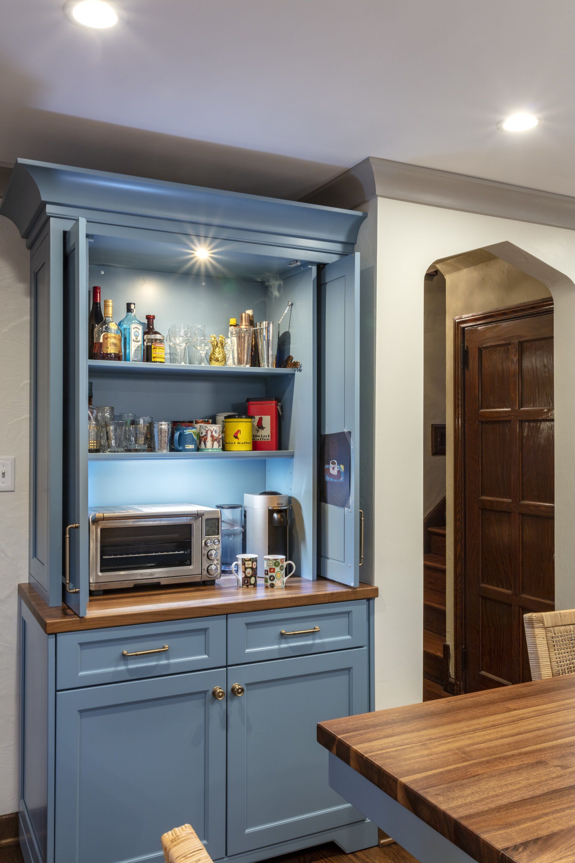 Blue kitchen hutch with shelves, microwave, and cabinets beside a wooden dining table.