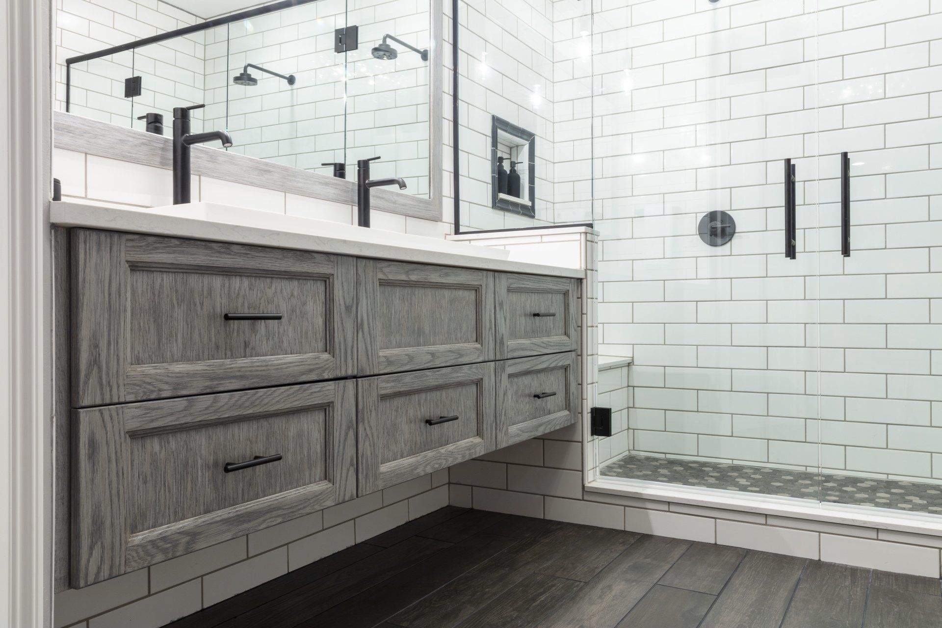 Modern bathroom with gray vanity, black fixtures, white tile shower, and glass shower enclosure