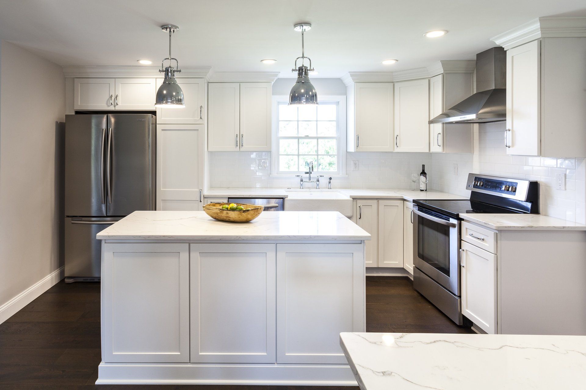 Modern white kitchen with island, stainless steel appliances, pendant lights, and a bowl of fruit