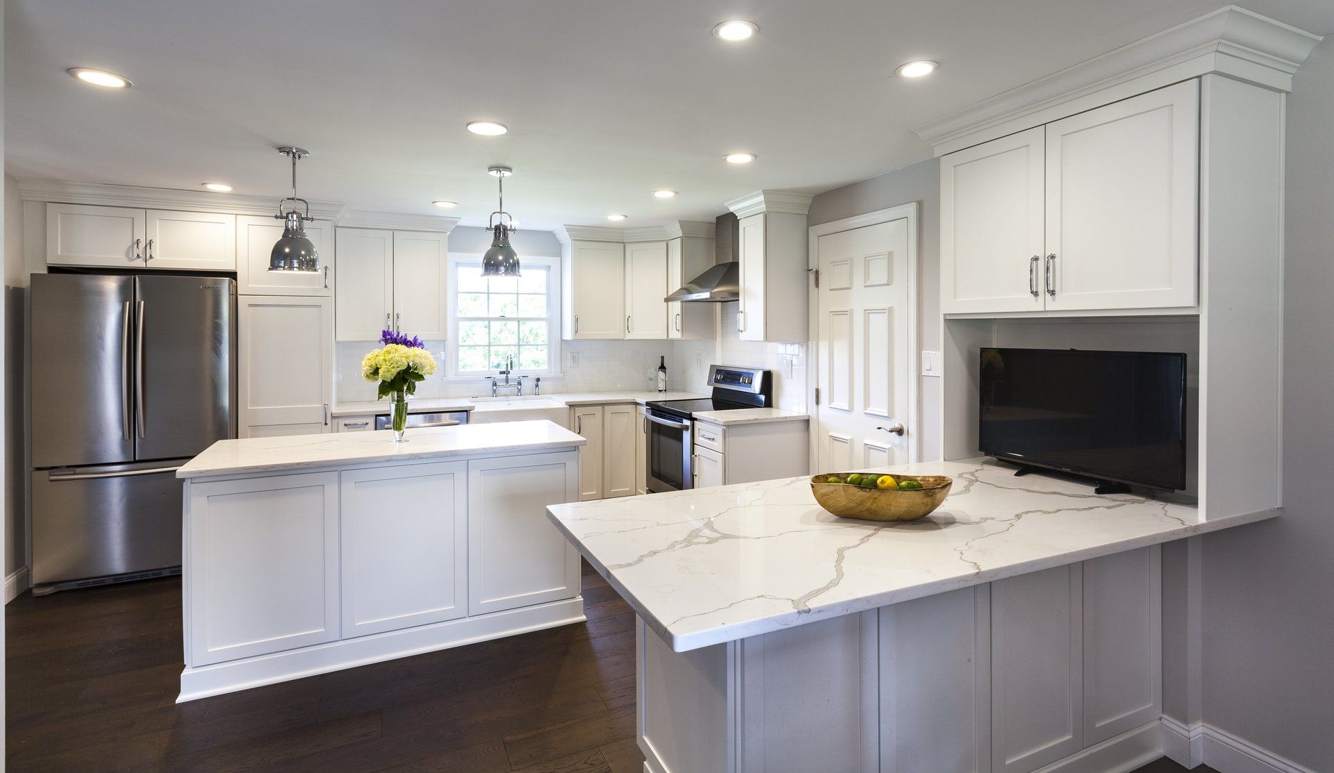 Bright modern kitchen with white cabinets, marble island, stainless fridge, and recessed lighting