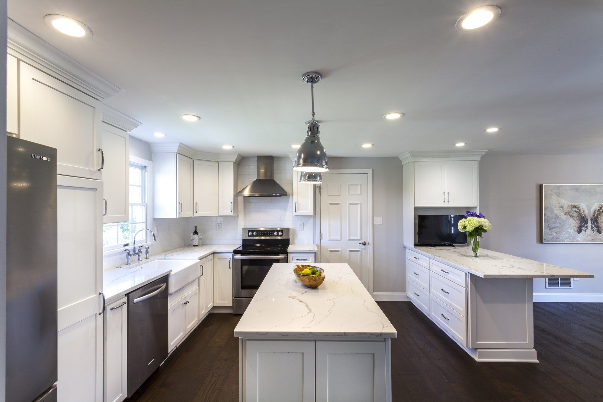 Bright modern kitchen with white cabinets, island, stainless appliances, and dark wood floor