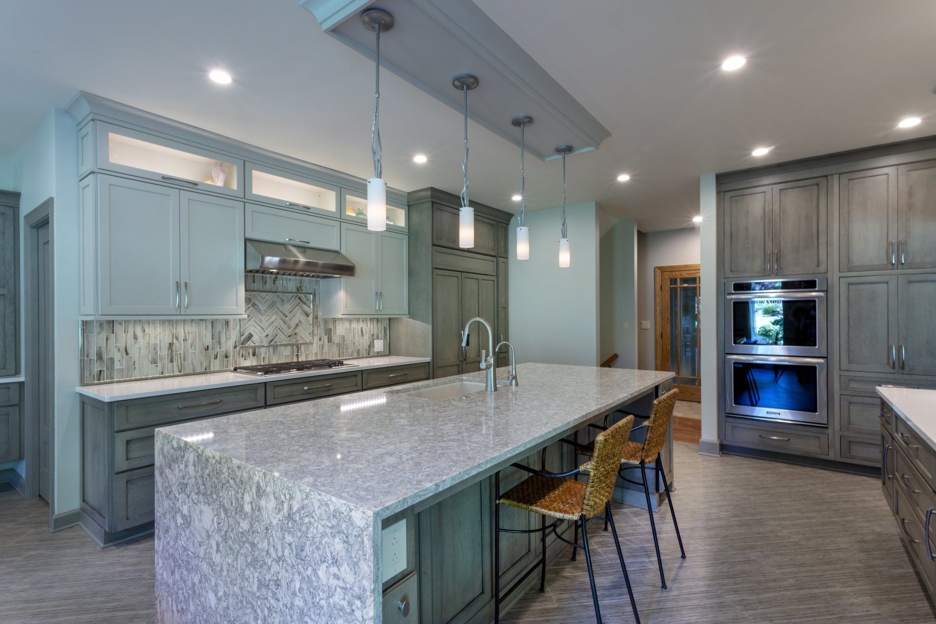Modern kitchen with a large stone island, gray cabinetry, and built-in double ovens