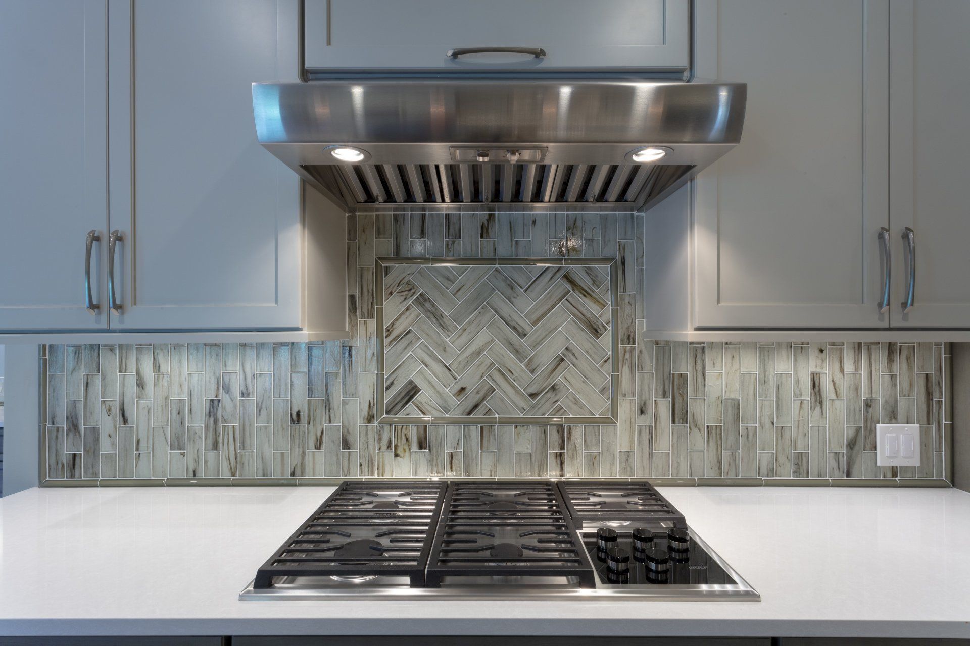 Modern kitchen with stainless steel range hood, gas cooktop, gray cabinets, and mosaic tile backsplash