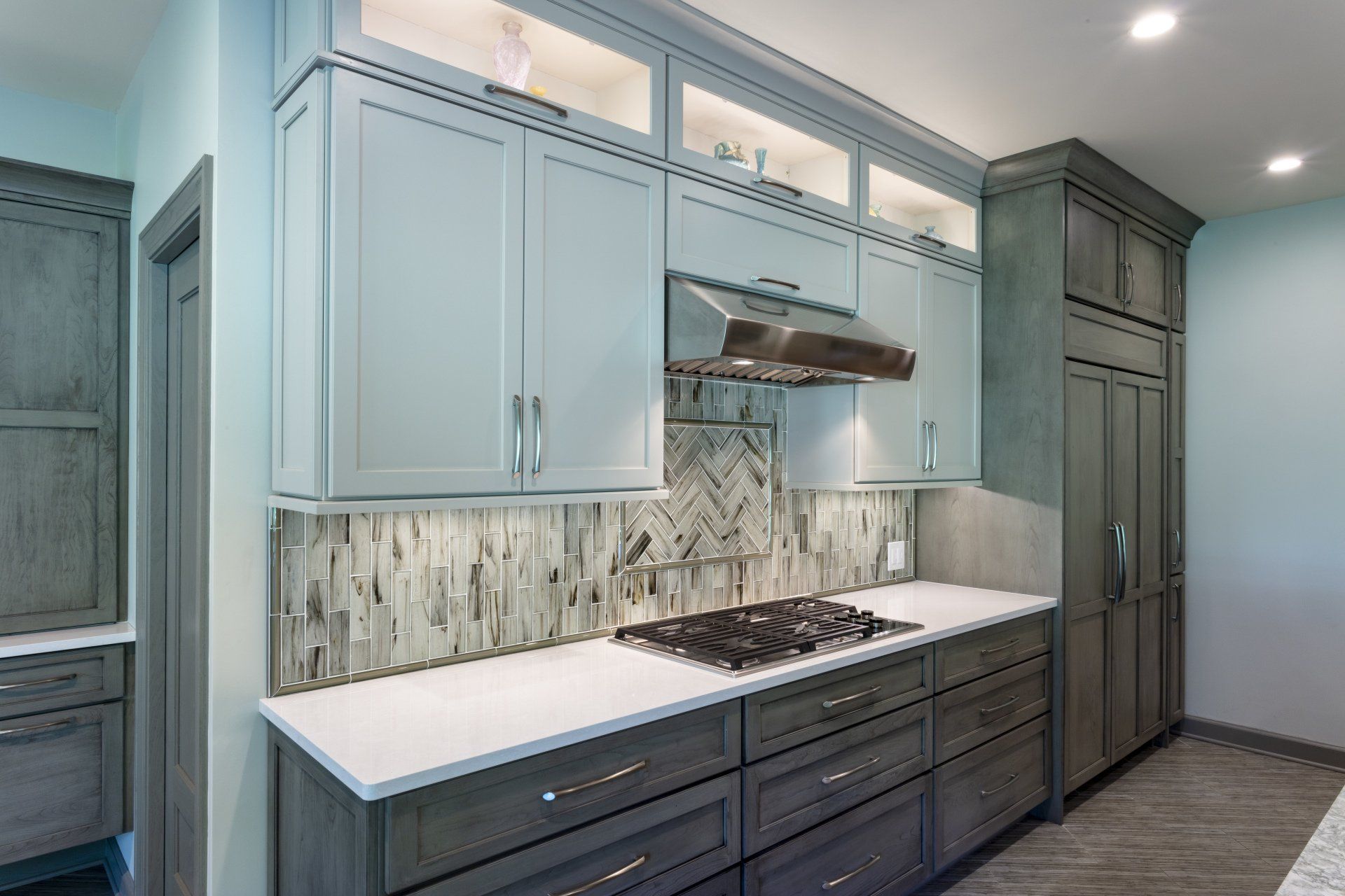 Modern kitchen with light blue cabinets, dark lower cabinets, white countertops, and stainless steel range hood.